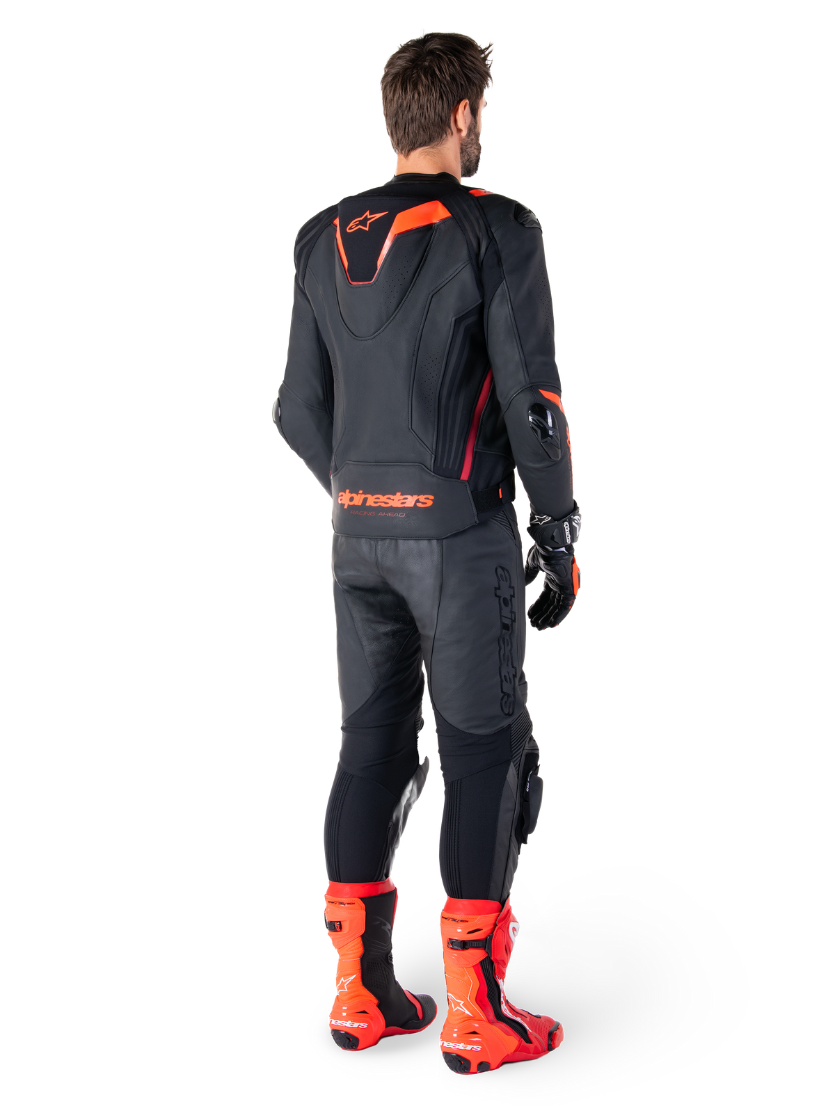 Alpinestars Missile V3 Ignition Leather Jacket, giacca da moto racing sportiva, nero e rosso fluo, vista posteriore di un pilota con completo da gara, pantaloni in pelle coordinati, guanti e stivali rossi, caratterizzata da gobba sportiva Aero-hump e logo sulla parte bassa della schiena.