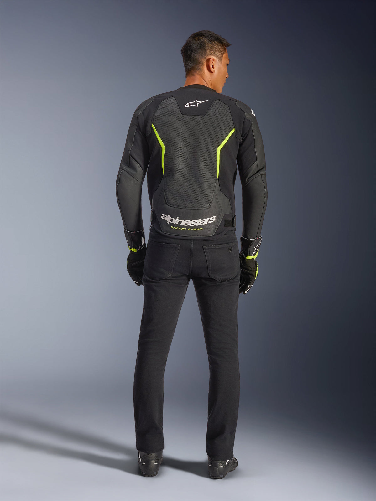 Giacca in pelle Alpinestars GP Force V2 Air, nero e giallo fluo, vista posteriore del modello che indossa la giacca sportiva da moto, con ampie sezioni traforate, dettagli giallo neon e logo 'alpinestars' bianco sulla parte bassa della schiena, abbinata a abbigliamento tecnico nero