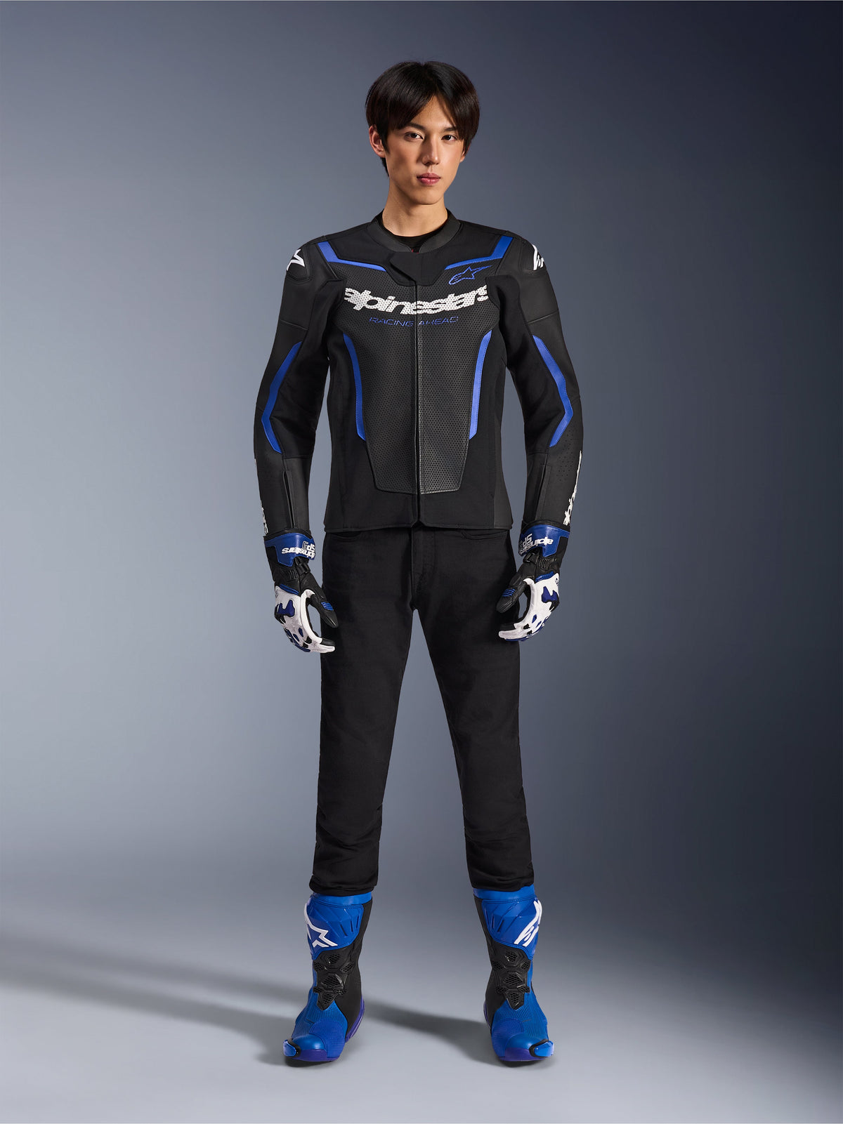 Giacca in pelle Alpinestars GP Force V2 Airflow in Nero Blu Metallizzato, indossata con guanti da corsa coordinati, pantaloni neri e stivali blu, abbigliamento tecnico professionale da motociclismo sportivo, inquadratura a figura intera in studio