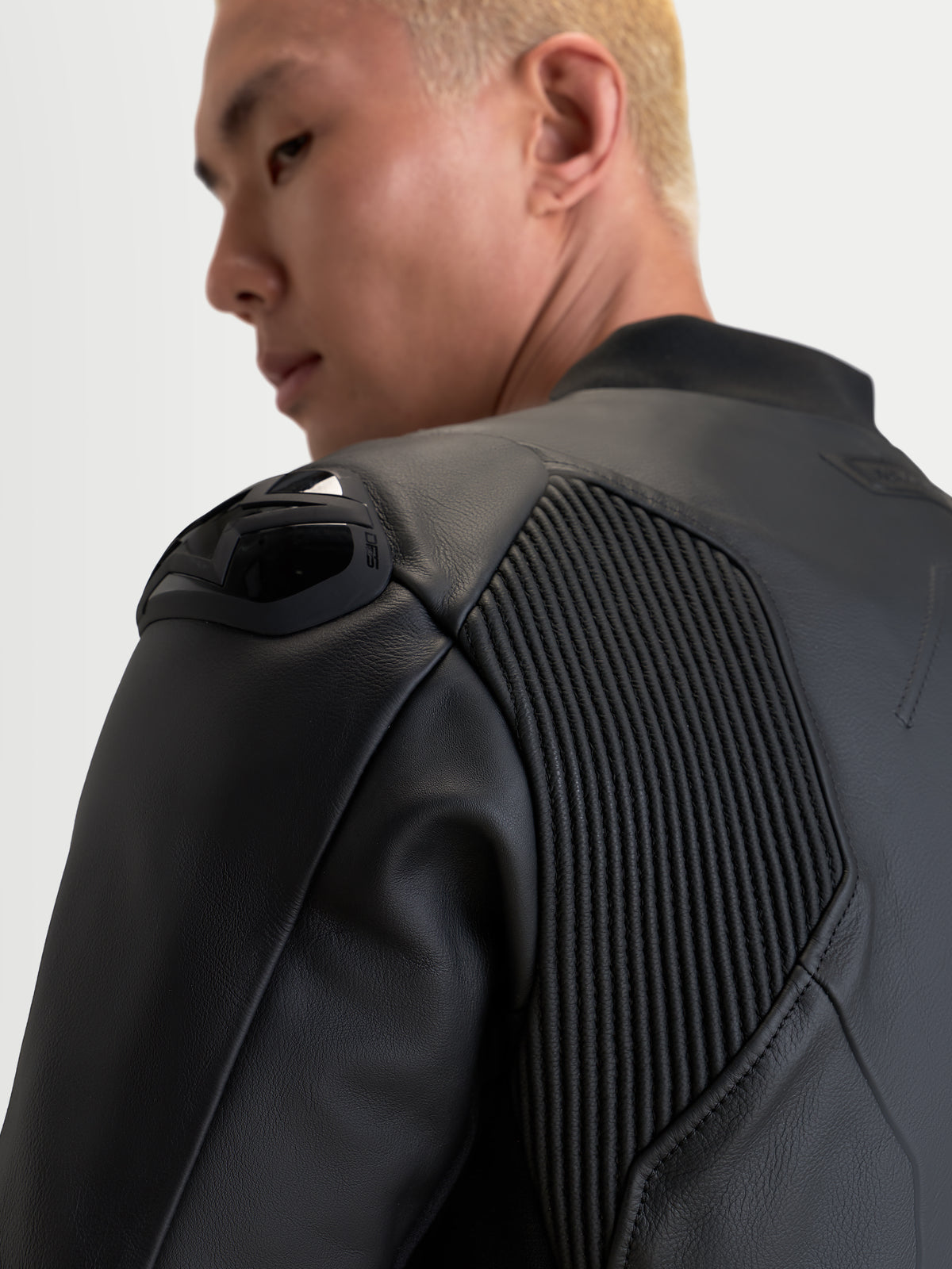 Alpinestars Caliber V 2 Giacca di pelle, giacca da moto in pelle nera, dettaglio ravvicinato delle protezioni sulle spalle e dei pannelli elastici a fisarmonica, indossata da un pilota