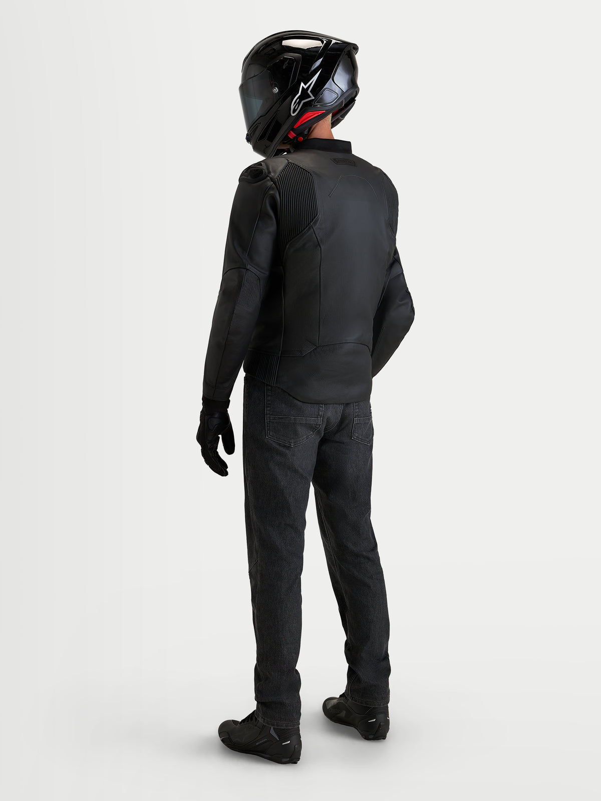 Alpinestars Caliber V 2 Giacca di pelle, giacca da moto sportiva in pelle nera da uomo, vista posteriore di un pilota con equipaggiamento completo, casco e jeans neri