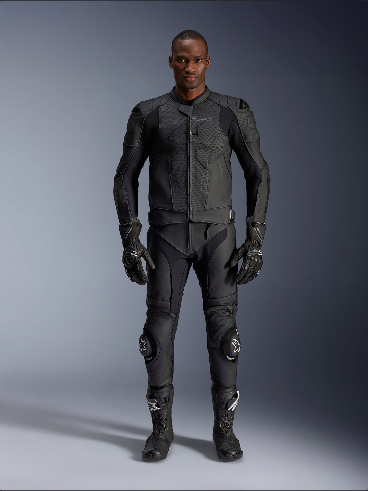 Giacca in pelle Alpinestars Dusk Airflow, nera, indossata con pantaloni da moto, guanti e stivali coordinati, caratterizzata da pelle traforata per il massimo flusso d'aria, design ergonomico multi-pannello e protezioni interne, abbigliamento professionale per guida sportiva e su strada