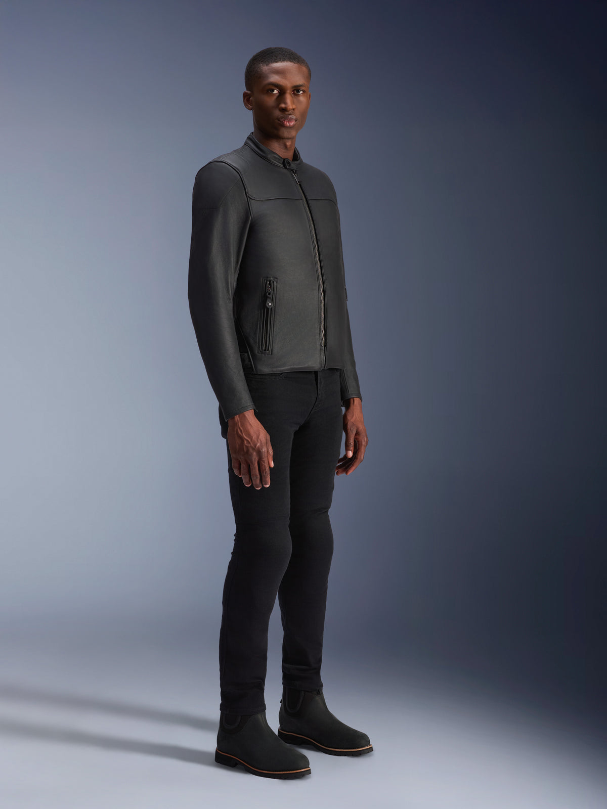 Modello che indossa la giacca in pelle Alpinestars Blacktrack, nero su nero, stile biker moderno in pelle premium con dettagli delle zip metalliche, abbinata a pantaloni e stivali neri per un look urbano contemporaneo