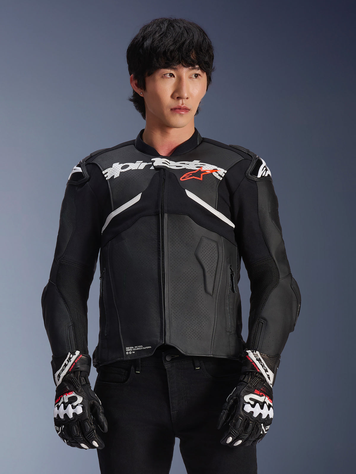 Alpinestars Atem V5 Leather Jacket, giacca da moto racing, nera con accenti bianchi e rossi, costruzione in pelle premium con protezioni rinforzate, indossata con guanti da corsa coordinati