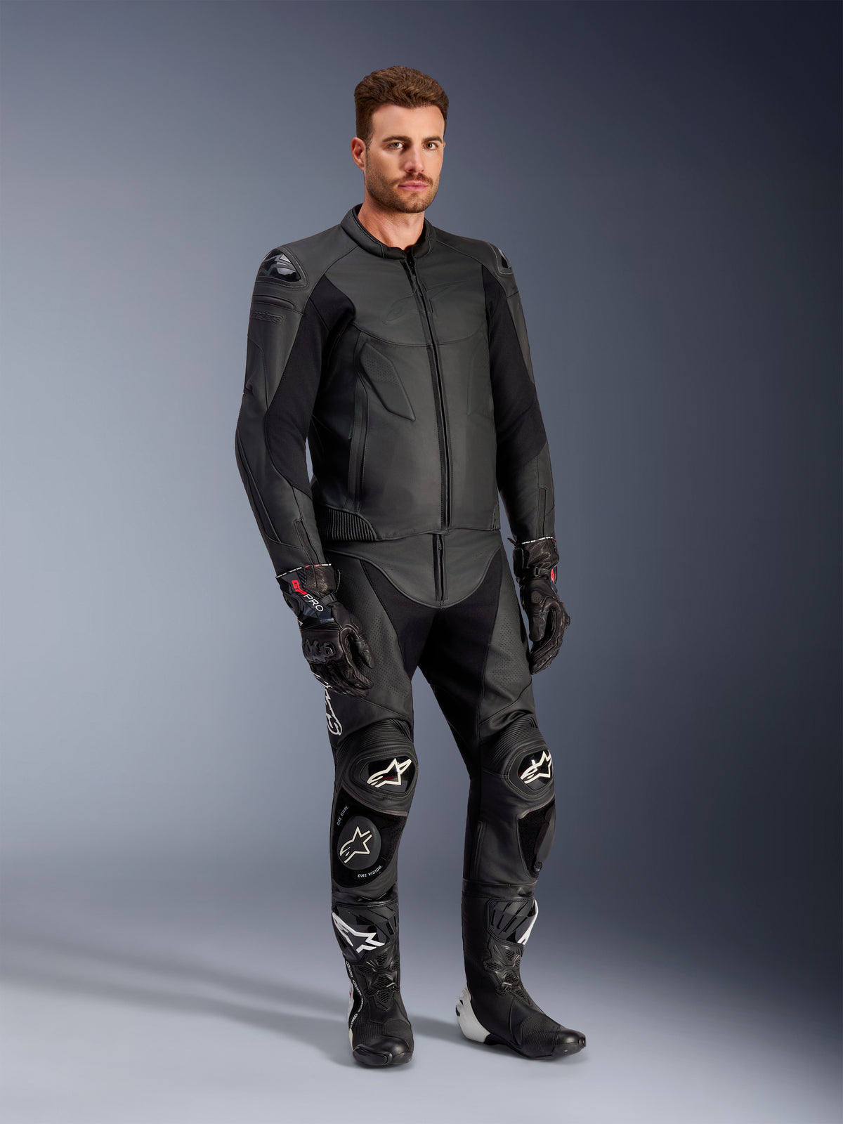Modello che indossa la giacca in pelle Alpinestars Caliber in nero, abbinata a pantaloni da moto in pelle nera coordinati, guanti racing e stivali, mostrando un outfit completo da strada sportivo.