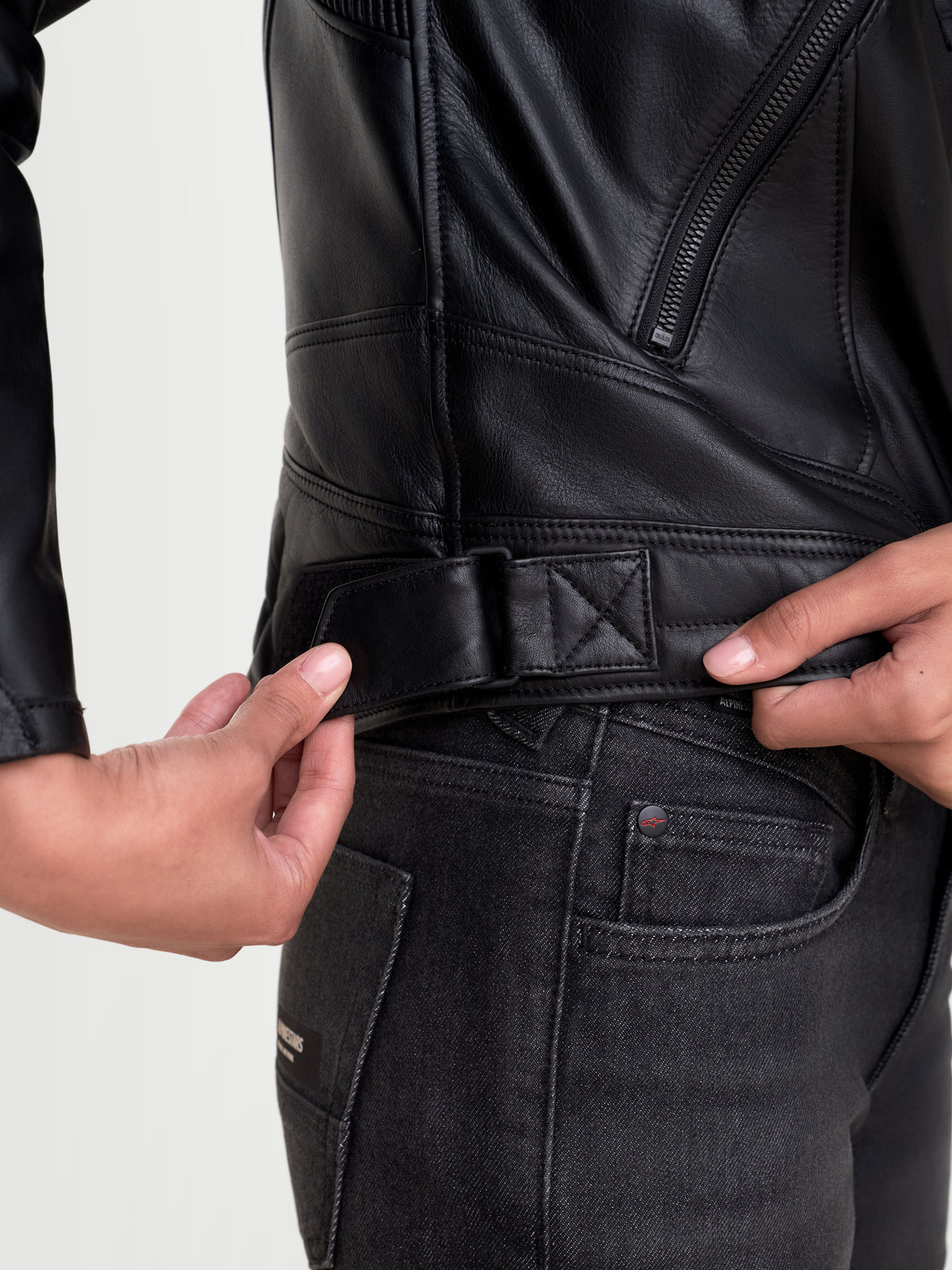 Alpinestars Revea Donna Giacca di pelle, giacca da moto urbana in pelle nera, vista ravvicinata della linguetta di regolazione in vita e della struttura in pelle bovina pieno fiore indossata da una modella