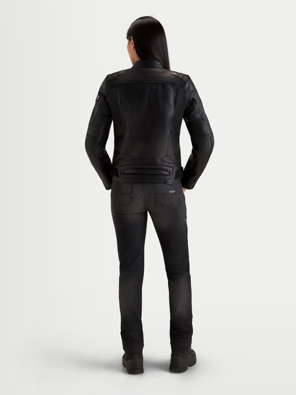 Alpinestars Revea Donna Giacca di pelle, giacca da moto urban da donna in pelle, vista posteriore su una modella con jeans scuri e stivaletti, struttura in pelle bovina pieno fiore