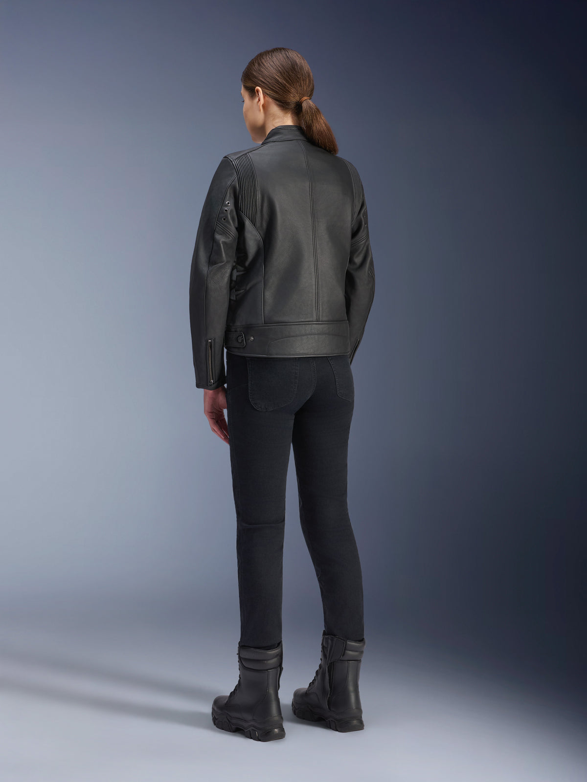 Giacca in pelle Stella Dyno Alpinestars, giacca da moto da donna, nera, vista posteriore che mostra la costruzione in pelle pregiata e la vestibilità sagomata, indossata con pantaloni da guida neri e stivali neri, stile urban riding