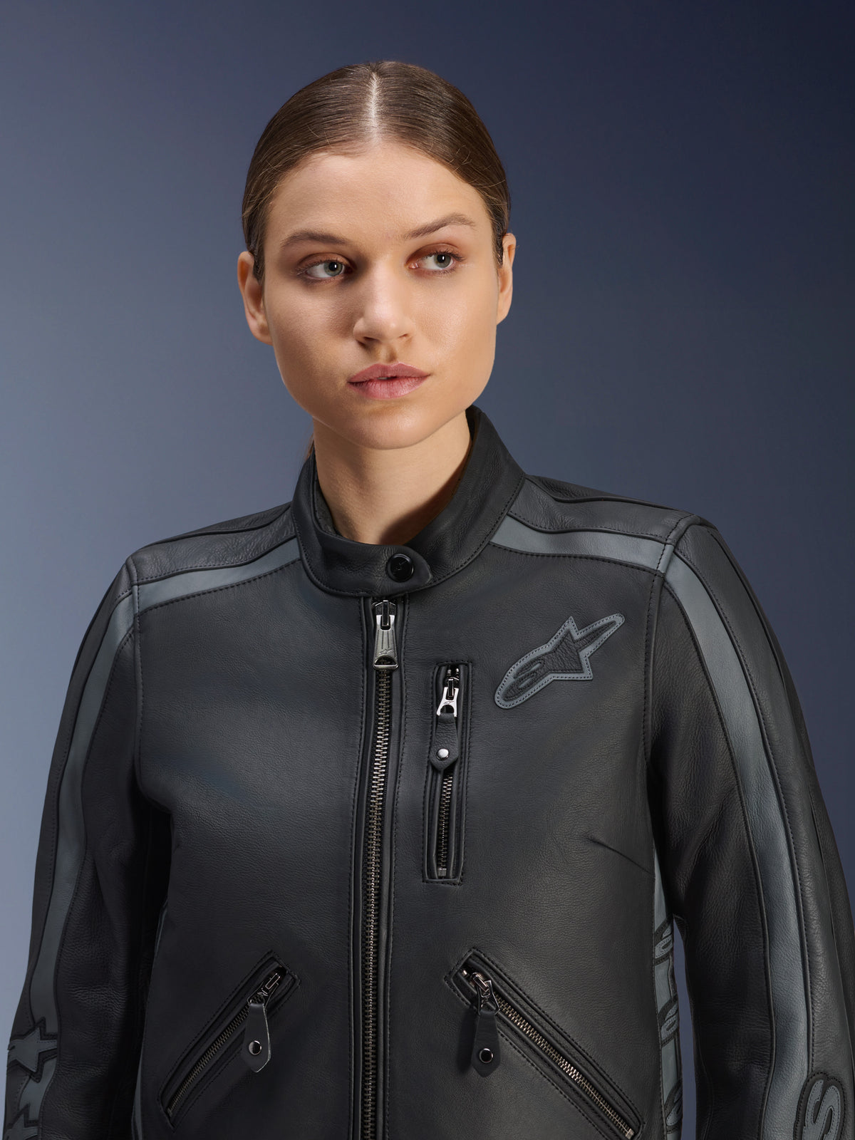Modella che indossa la giacca in pelle Alpinestars Stella Dyno in Black Tar Gray Dark Gray, giacca da moto in pelle bovina premium dal design heritage, con dettagli grigi sulle spalle e tasche multiple con zip, progettata per una vestibilità specifica femminile.