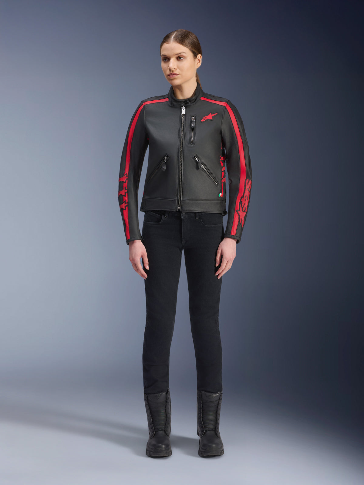Giacca in pelle Alpinestars Stella Dyno, giacca da moto da donna, nero e rosso Haute Red, con strisce racing rosse su spalle e maniche, logo a stella rosso sul petto, indossata con pantaloni slim-fit neri e stivali, pelle bovina premium dal design heritage moderno