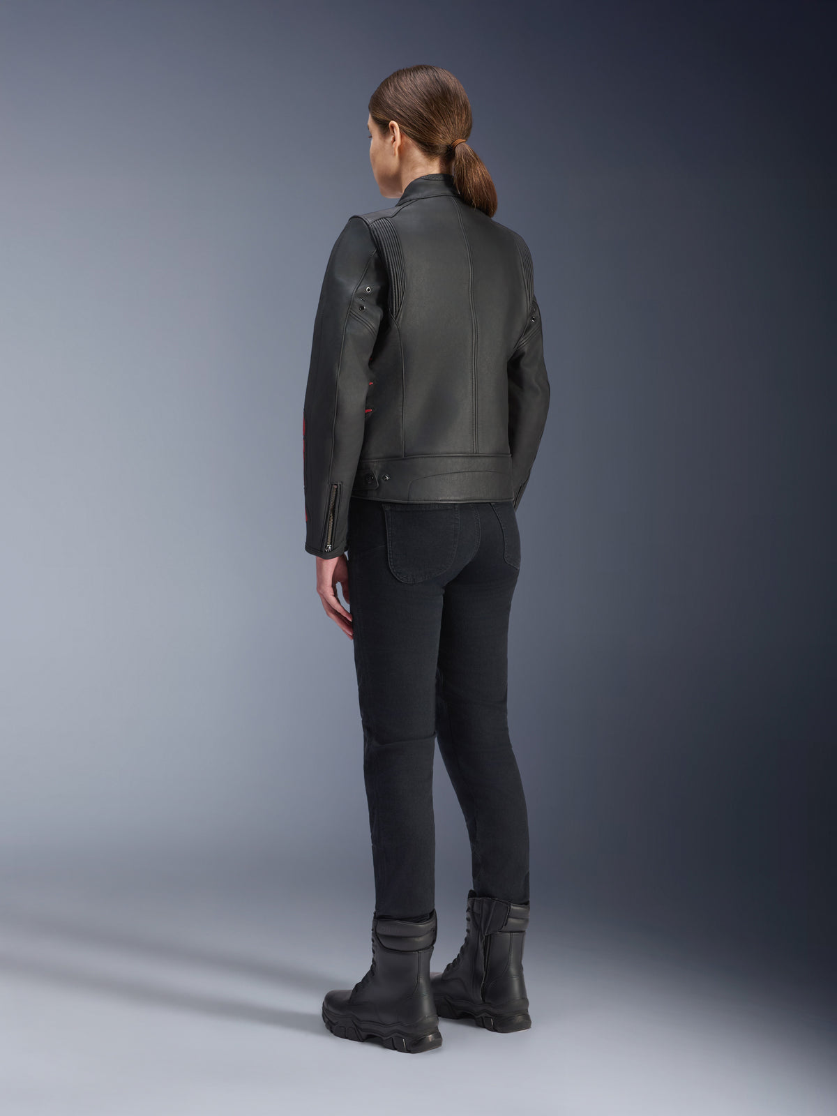 Giacca in pelle Alpinestars Stella Dyno, giacca da moto da donna, Nero Haute Red, vista posteriore, indossata con pantaloni da moto neri e stivali neri, finitura in pelle premium con stile heritage