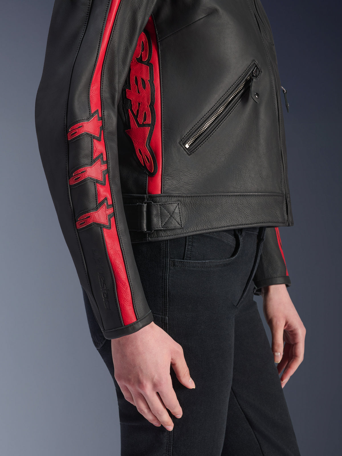 Giacca in pelle Alpinestars Stella Dyno, giacca da moto da donna, nero e rosso Haute Red, vista laterale indossata da una modella, caratterizzata da strisce rosse con loghi a stella sulla manica e grande logo rosso laterale, pelle bovina premium, stile urban riding
