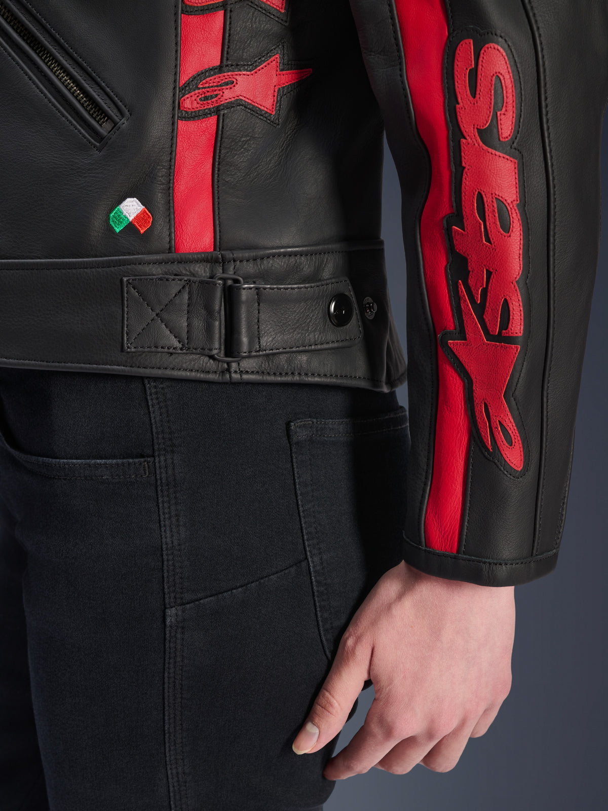 Giacca in pelle Stella Dyno Alpinestars, giacca da moto in pelle da donna, nero e rosso Haute Red, vista ravvicinata di vita e manica, strisce racing rosse con marchio Alpinestars, cinghia regolabile in vita, piccolo ricamo della bandiera italiana, costruzione in pregiata pelle bovina