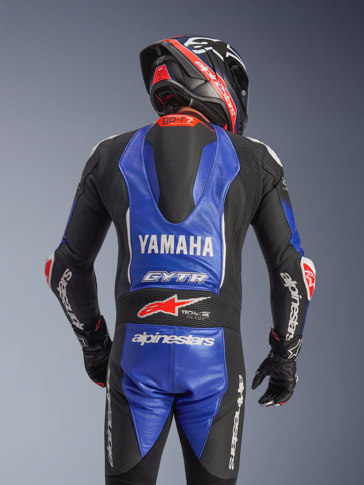 Tuta intera in pelle Alpinestars Yamaha GP-R7, vista posteriore, blu metallizzato e nero con accenti bianchi e rossi, branding Yamaha e GYTR ben visibile, dotata di gobba aerodinamica, indossata con casco e guanti da corsa coordinati per un look professionale pronto per la pista
