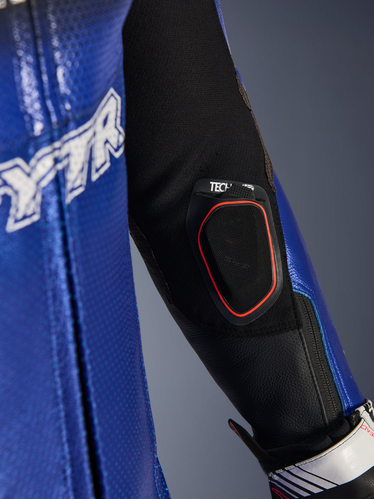 Dettaglio dell'avambraccio della tuta in pelle Yamaha GP-R7 1PC, tasca integrata per display Bluetooth Tech-Air 10 con bordo rosso, pelle traforata blu metallizzato e inserti in tessuto elasticizzato nero per prestazioni racing.
