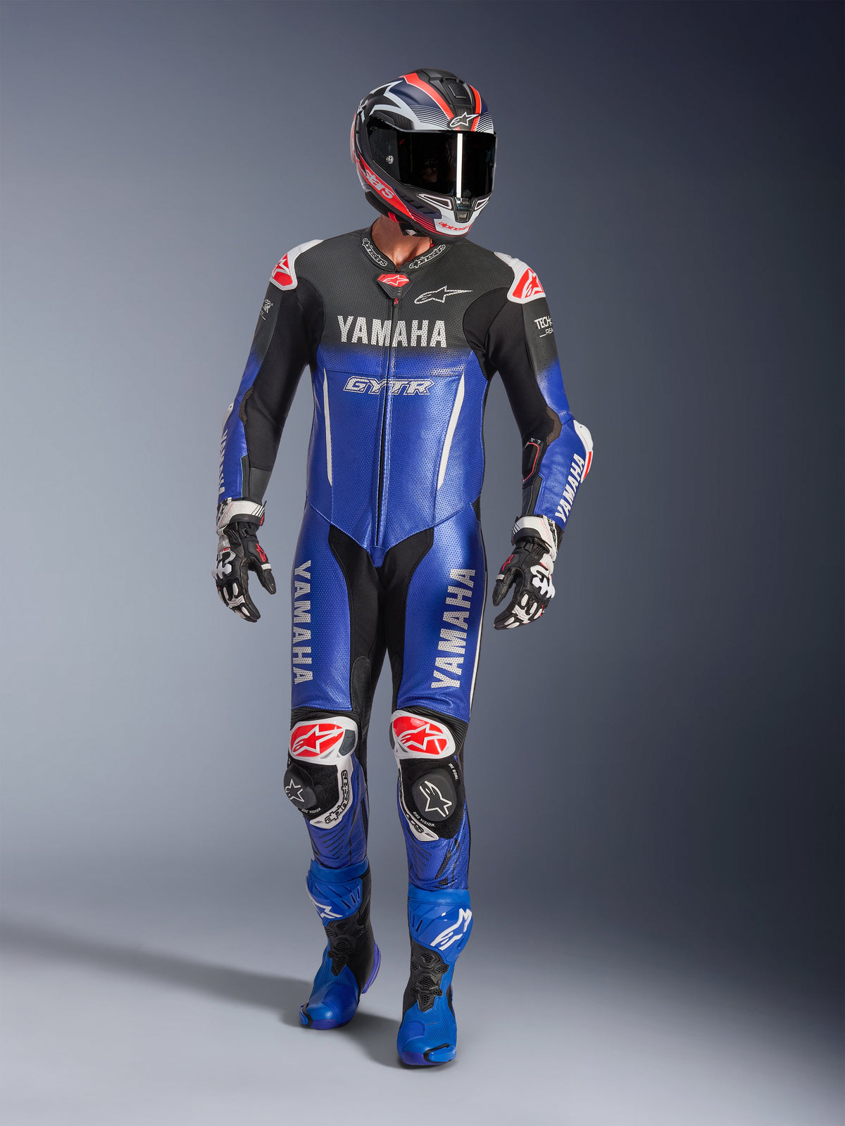 Alpinestars Yamaha GP-R7 One Piece Leather Suit, tuta da corsa in pelle monopezzo, blu metallizzato e nero con dettagli rossi e bianchi, loghi Yamaha e GYTR, indossata con casco, guanti da corsa e stivali blu abbinati, equipaggiamento professionale ad alte prestazioni