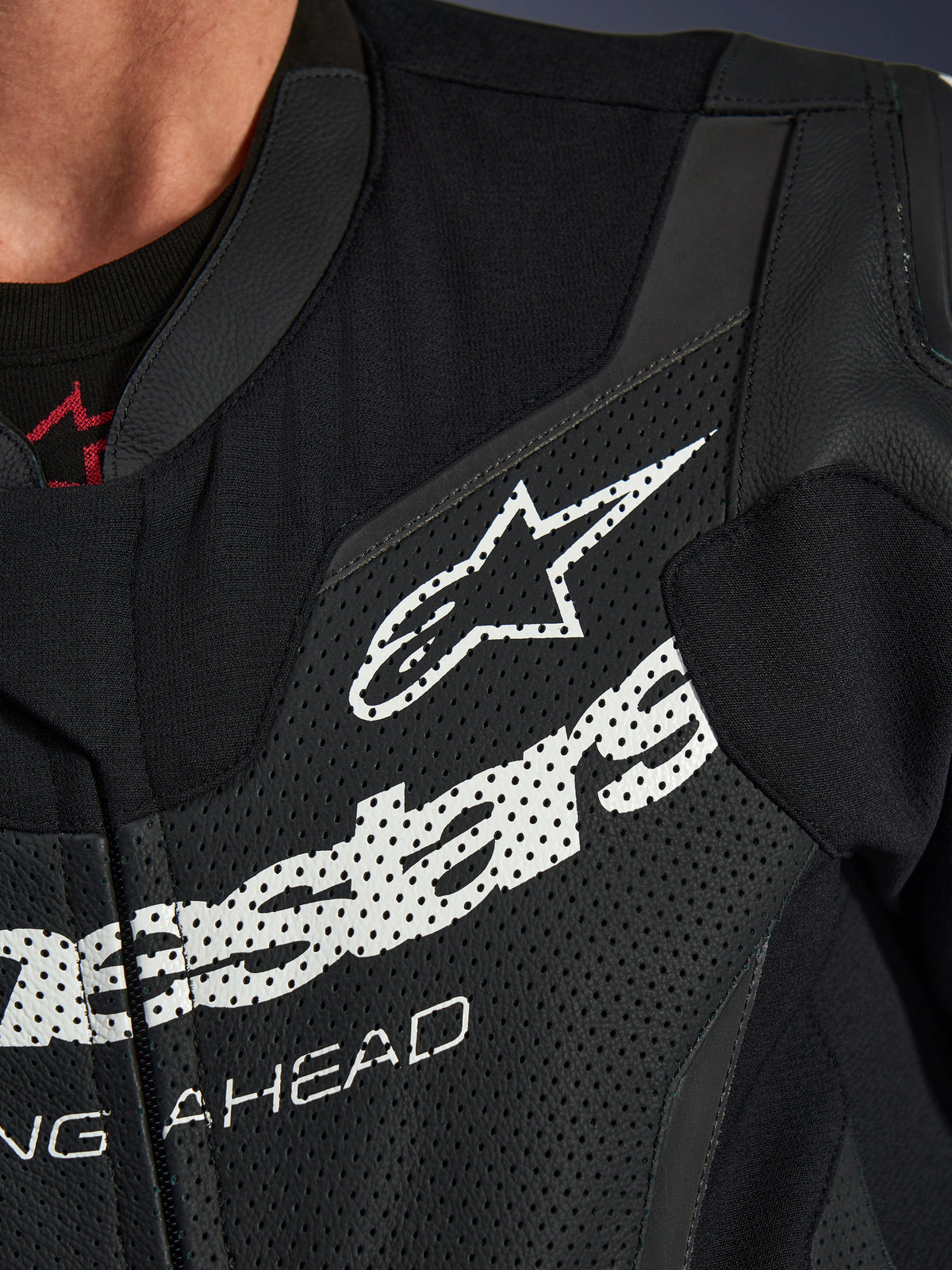 Tuta in pelle monopezzo Alpinestars GP Force V2, primo piano della zona del petto, pelle traforata nera con grande logo Alpinestars bianco, abbigliamento tecnico da guida sportiva, dettagli della texture e del branding