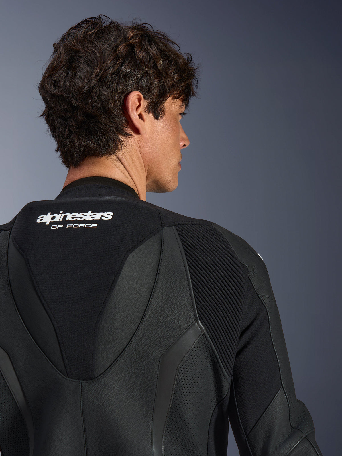 Alpinestars GP Force V2 Leather Suit monopezzo, nero, vista ravvicinata della parte superiore della schiena e della gobba aerodinamica, con logo bianco, sezioni in pelle traforata e pannelli elasticizzati a fisarmonica per prestazioni da gara.
