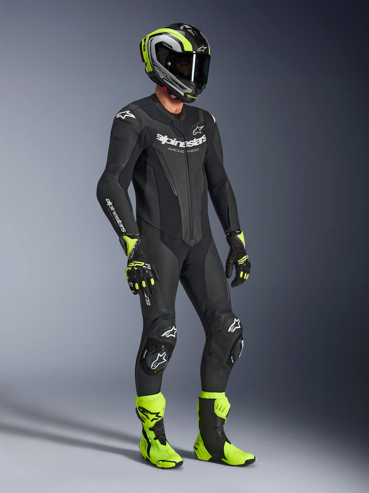 Tuta in pelle Alpinestars GP Force V2, tuta da moto monopezzo, nera con marchio bianco, indossata con casco, guanti e stivali coordinati in giallo neon e nero, abbigliamento racing ad alte prestazioni per pista e guida sportiva