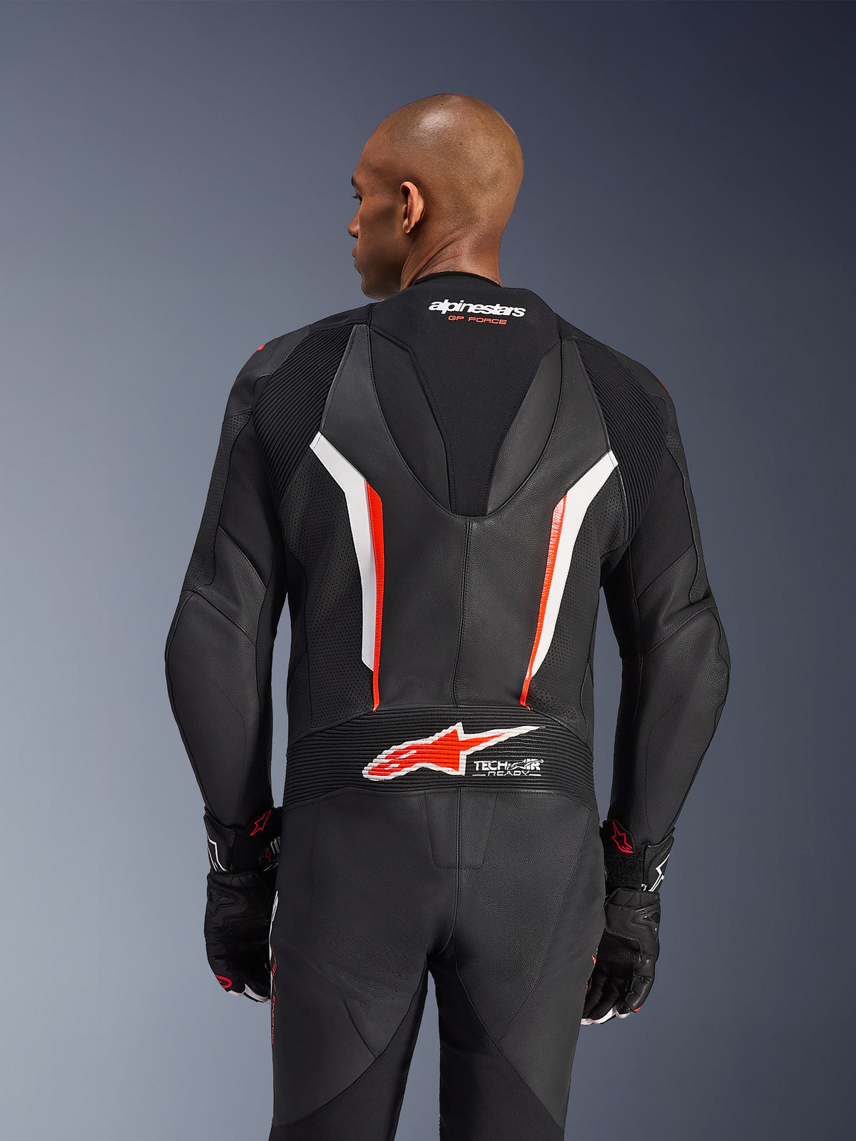 Tuta in pelle Alpinestars GP Force V2, tuta da moto intera, nero, bianco e rosso fluo, vista posteriore della parte superiore del corpo che mostra la pelle traforata e il logo Tech-Air Ready, indossata con guanti coordinati neri e rossi