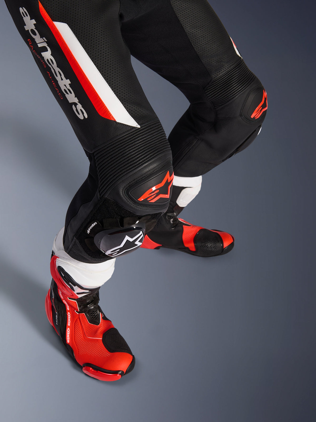 Alpinestars GP Force V2 1-Piece Leather Suit, nero, bianco e rosso fluo, primo piano di gambe e ginocchia con protezioni DFS Lite e saponette sostituibili, abbinata a stivali da racing professionali
