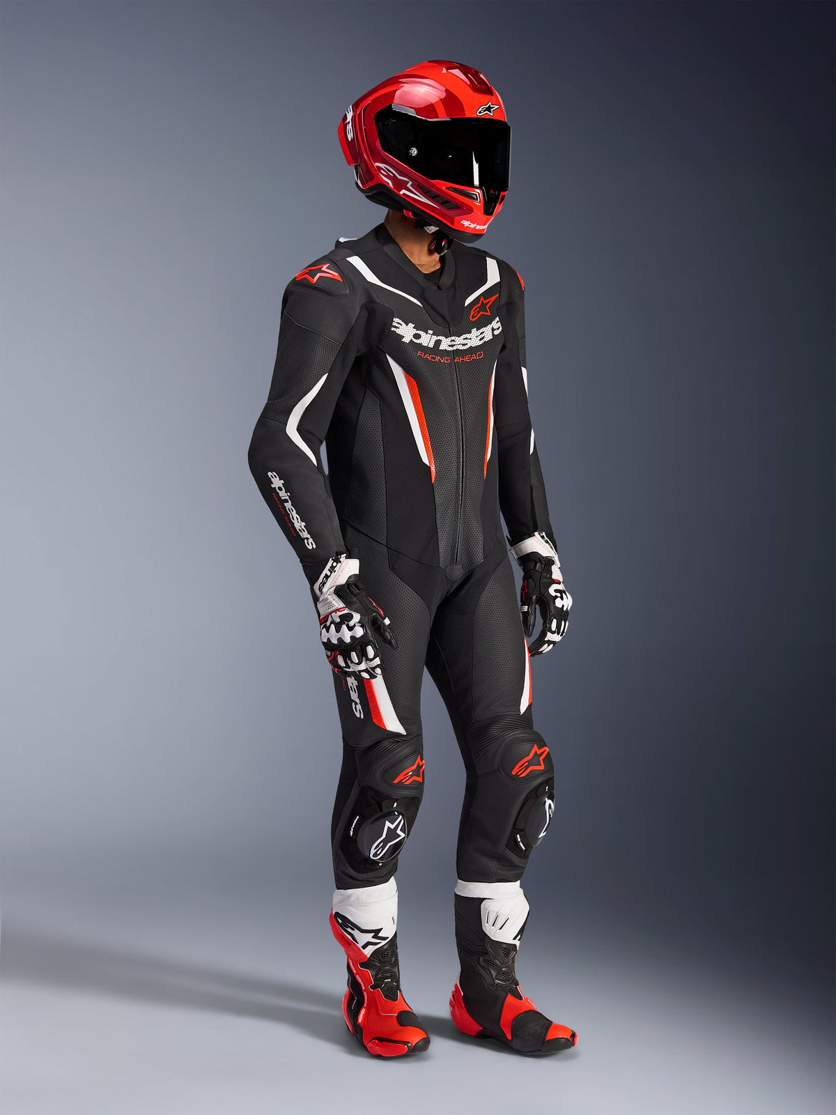 Tuta in pelle Alpinestars GP Force V2 - 1 Pezzo, tuta racing professionale in nero, bianco e rosso fluo, con pannelli in pelle traforata e scudi DFS Lite. Equipaggiamento completo da pista con casco racing rosso, guanti e stivali coordinati.