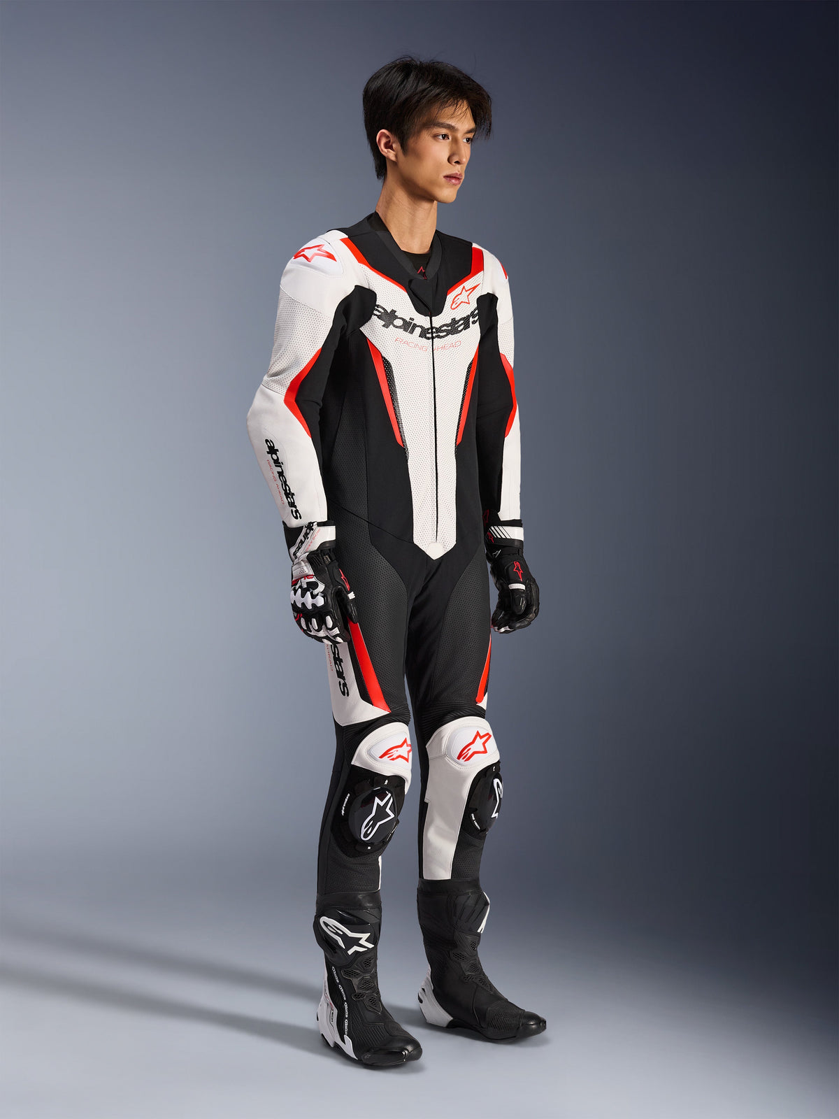 Alpinestars GP Force V2 Leather Suit - 1 Piece, tuta da moto racing monopezzo, bianco, nero e rosso fluo, indossata con guanti e stivali coordinati, con pelle traforata e marchio Alpinestars in evidenza, design aerodinamico per prestazioni in pista