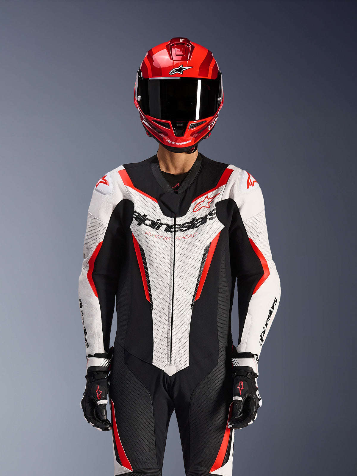 Alpinestars GP Force V2 Leather Suit - Monopezzo, Bianco Nero Rosso Fluo, indossata con casco integrale rosso e guanti da corsa neri, con pannelli in pelle traforata e logo Alpinestars sul petto, abbigliamento professionale per competizioni motociclistiche