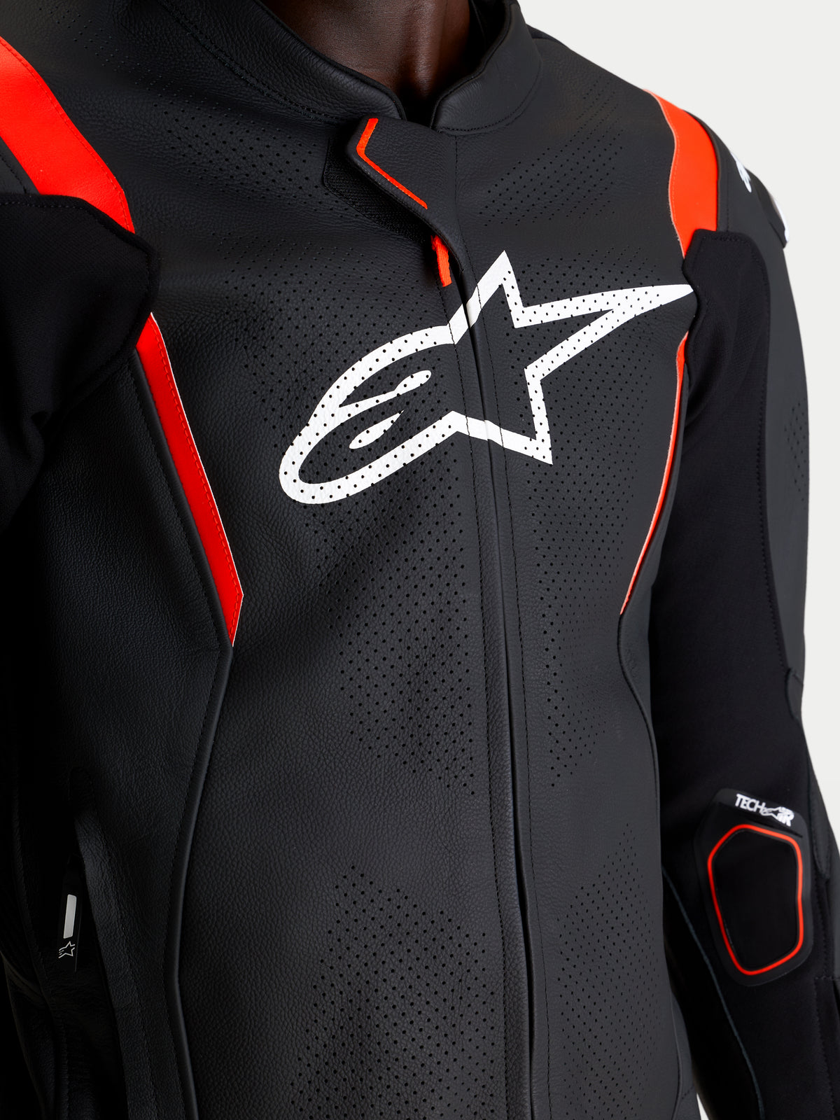 Alpinestars Missile V3 Tuta in pelle 2 Pc, primo piano della parte superiore del torace con logo Alpinestars bianco, struttura in pelle traforata da corsa, nero e rosso fluo, dettagli di protezione sulle braccia