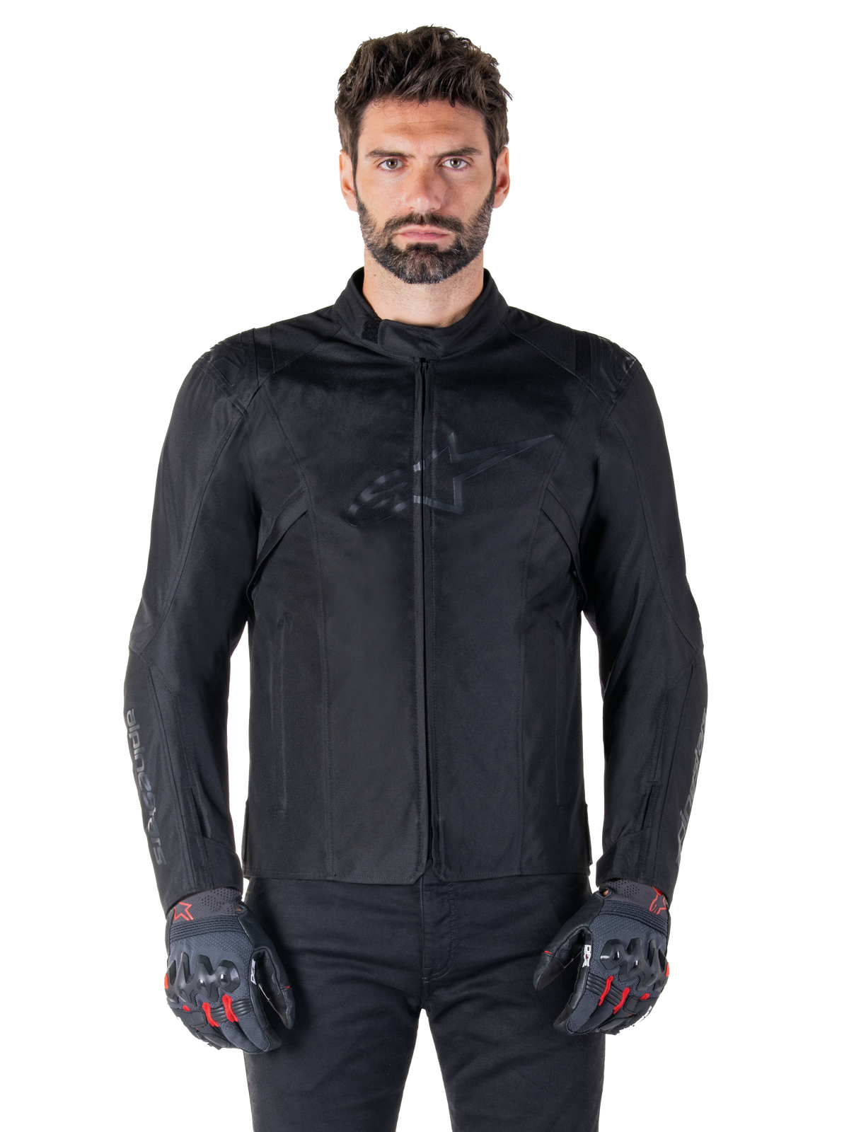 Giacca Alpinestars T-SPS V2 Waterproof, giacca da moto in tessuto nero, indossata da un pilota con guanti neri e rossi, dotata di colletto alto, zip frontale e logo discreto sul petto, protezione impermeabile per guida sportiva e urbana