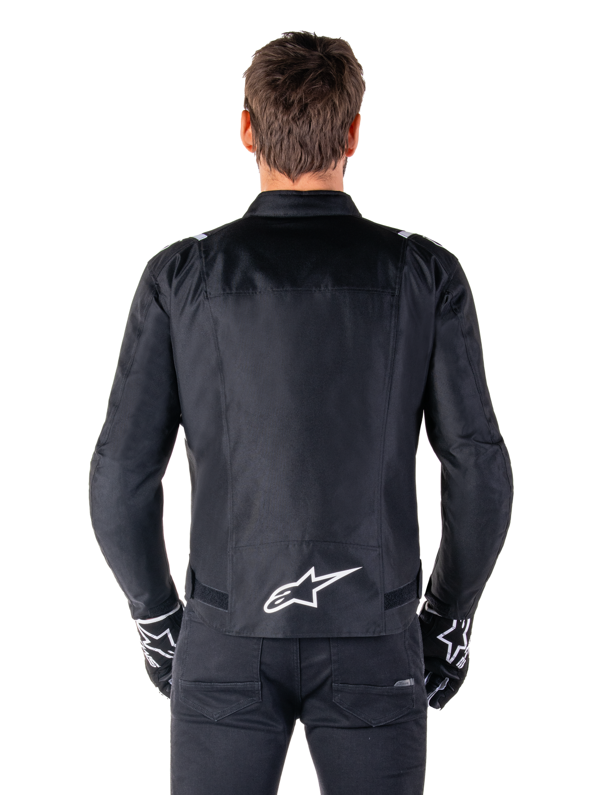 Giacca Alpinestars T-SPS V2 Waterproof, nero e bianco, vista posteriore con logo Alpinestars bianco sulla parte bassa della schiena, indossata con pantaloni e guanti neri, giacca da moto in tessuto con taglio sportivo