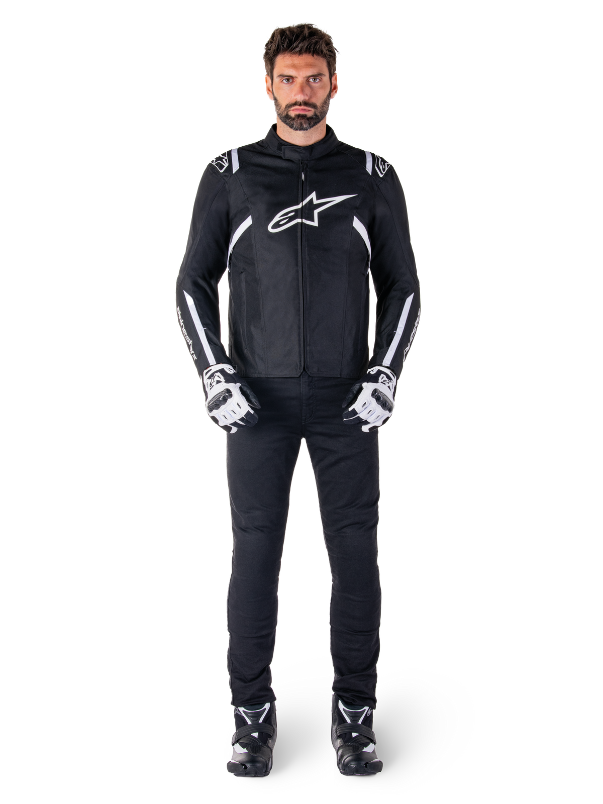 Giacca impermeabile Alpinestars T-SPS V2, nero e bianco, indossata da un modello uomo con pantaloni neri e guanti coordinati, con logo Alpinestars bianco sul petto e dettagli sulle maniche, silhouette dal taglio sportivo per la guida in moto in ogni condizione atmosferica
