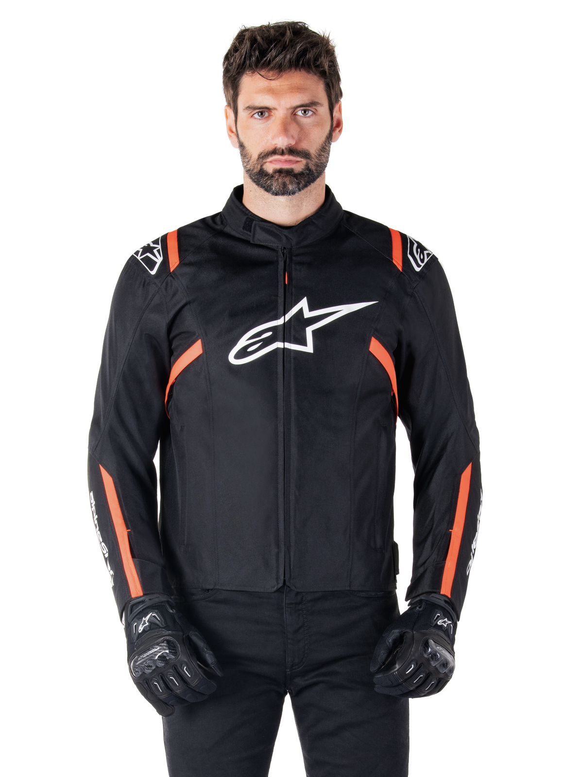 Giacca impermeabile Alpinestars T-SPS V2, nero, bianco e rosso fluo, indossata da un modello con guanti da moto neri, caratterizzata da un grande logo Alpinestars bianco sul petto e vivaci dettagli arancioni sulle spalle e sulle maniche.