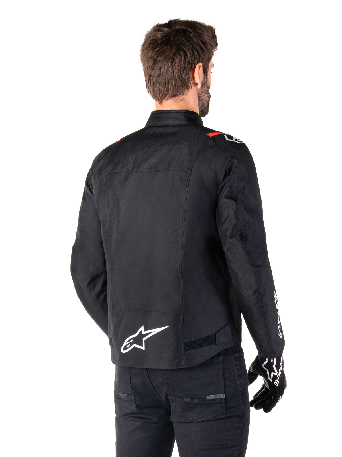 Giacca impermeabile Alpinestars T-SPS V2, nero bianco rosso fluo, vista posteriore, con logo Alpinestars bianco sulla parte bassa della schiena e dettagli rossi sulle spalle, indossata con guanti e pantaloni da moto neri, giacca da moto sportiva in tessuto.