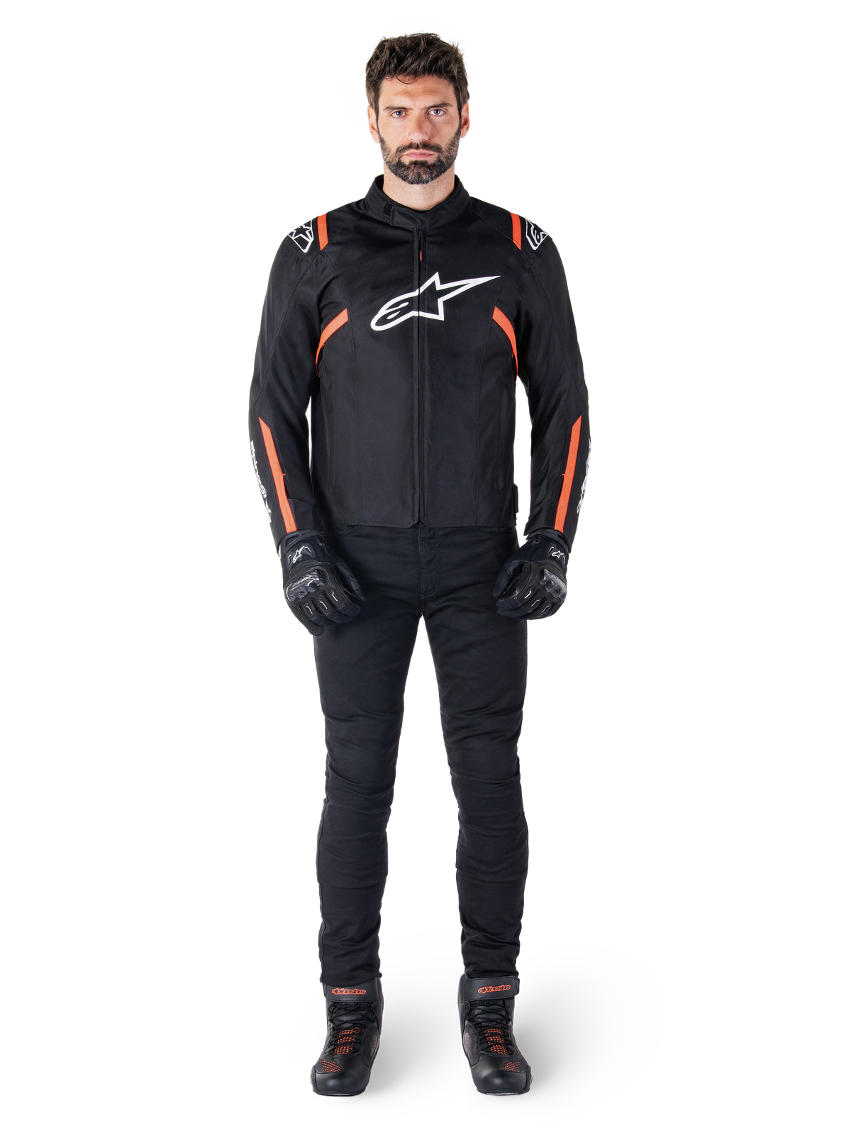 Modello che indossa la giacca Alpinestars T-SPS V2 Waterproof in Nero Bianco Rosso Fluo, abbinata a pantaloni da moto e guanti neri, con logo Alpinestars bianco sul petto e dettagli rossi sulle maniche.