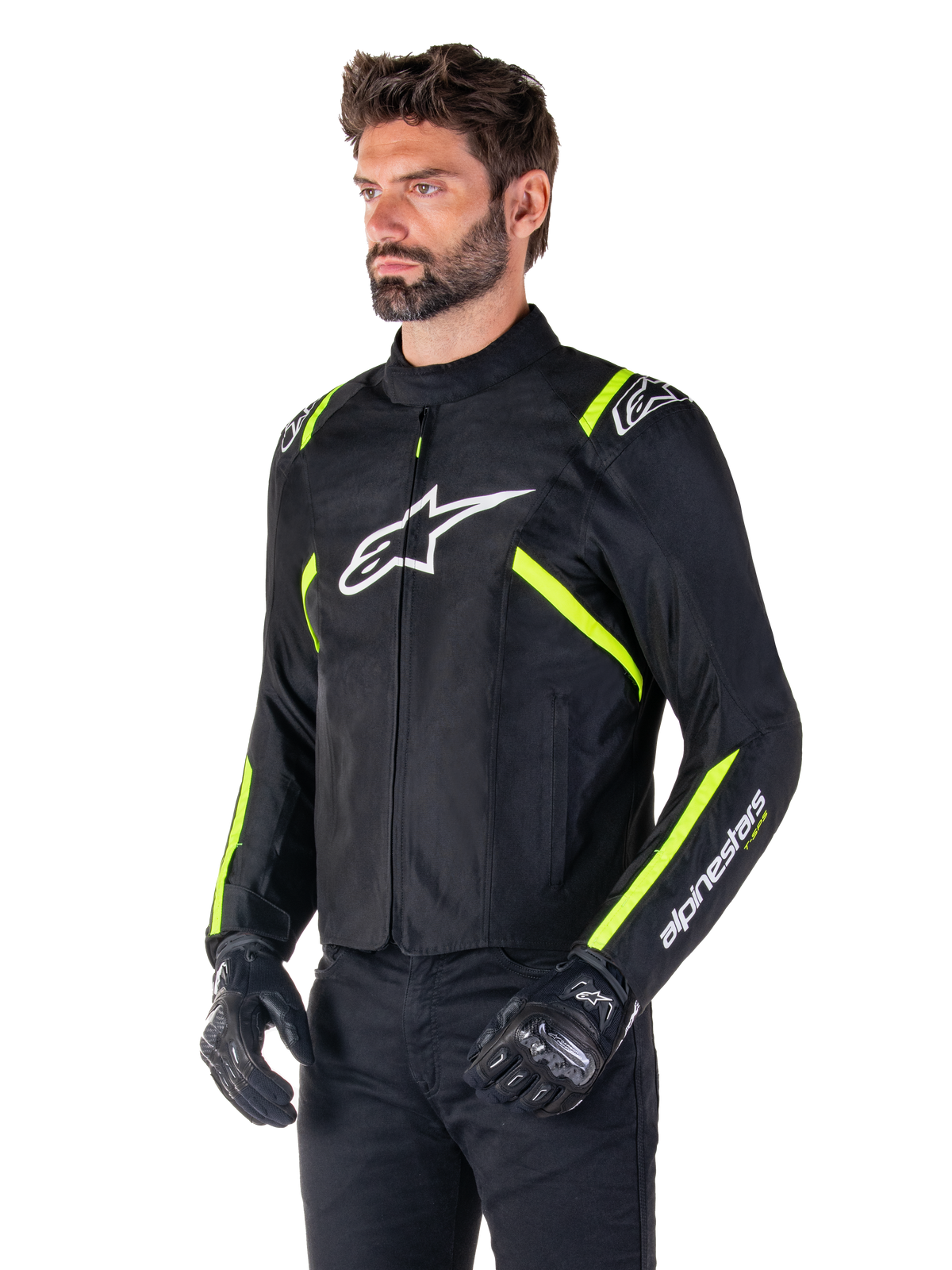 Modello che indossa la giacca impermeabile Alpinestars T-SPS V2, nero con dettagli bianco e giallo fluo, con logo Astars bianco sul petto e strisce giallo fluorescente su spalle e maniche, abbinata a pantaloni neri e guanti da guida, giacca da moto in tessuto dal taglio sportivo.