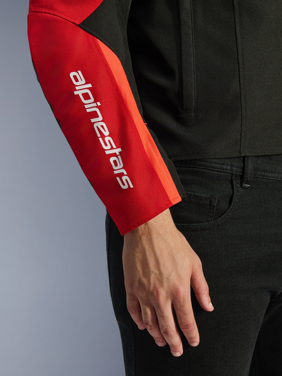 Alpinestars Giacca Impermeabile T-SPS V2, giacca da moto, nero e rosso, primo piano della manica con logo verticale bianco del brand su un pannello rosso, struttura in tessuto resistente con design d'ispirazione sportiva.