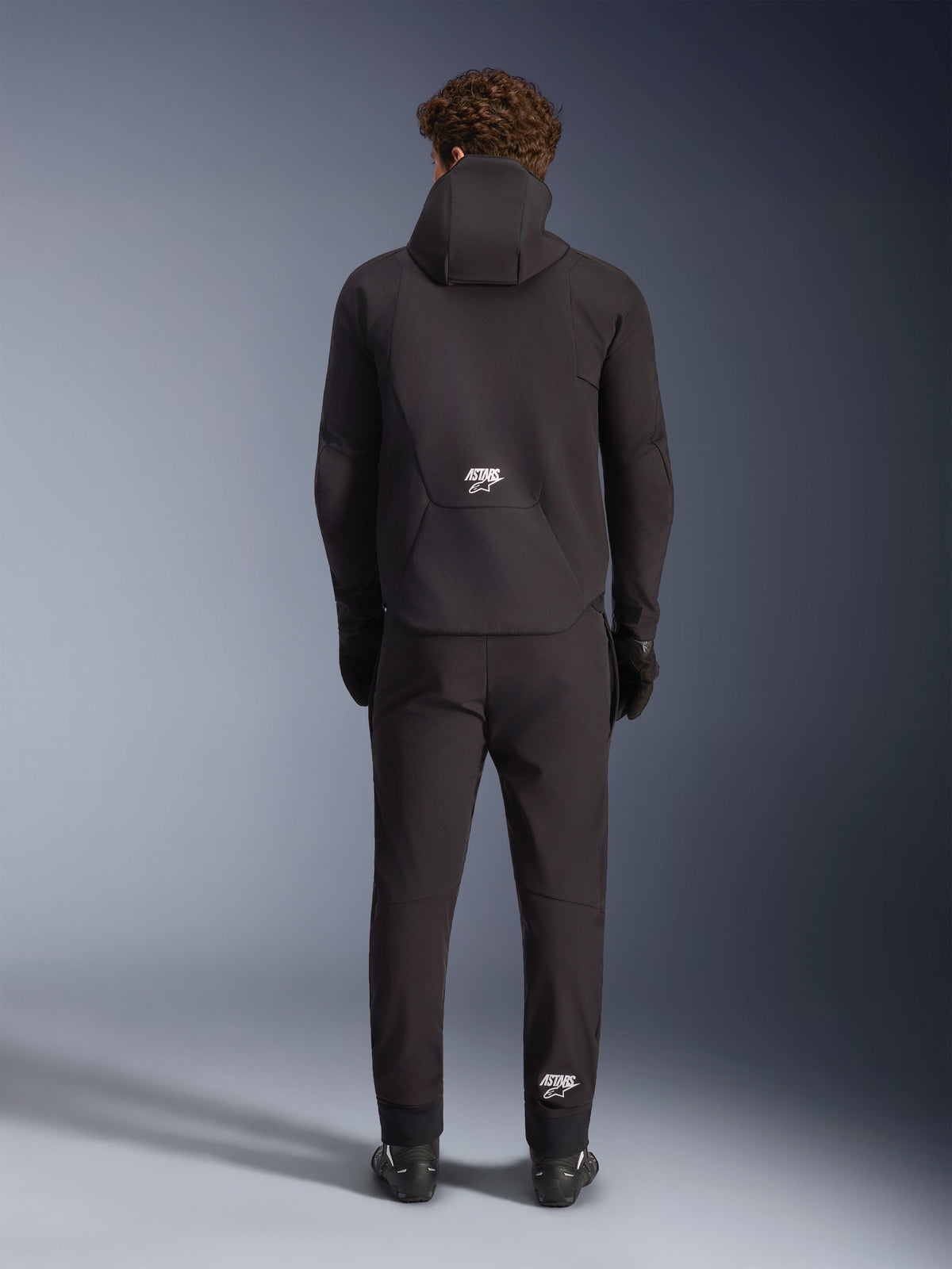 Alpinestars Giacca Aeroshell Impermeabile, giacca da moto softshell con cappuccio da uomo, nera, vista posteriore con logo ASTARS bianco, abbigliamento tecnico sportivo crossover