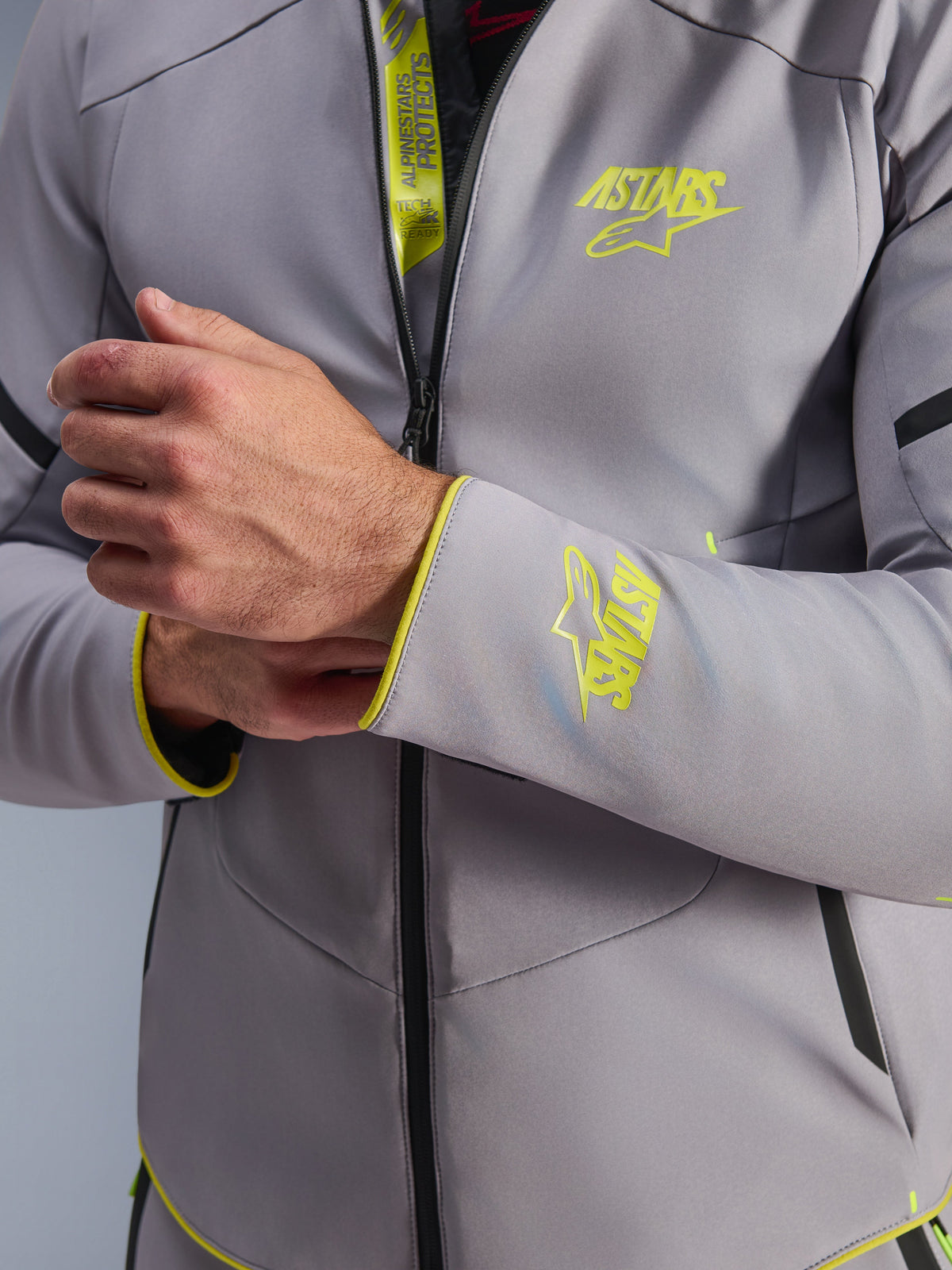 Giacca Alpinestars Aeroshell Waterproof, grigio medio con accenti giallo fluo, primo piano del petto e del polsino con loghi Astars giallo fluorescente, dettaglio dell'aletta interna con marchio Tech-Air Ready, moderna giacca da moto softshell sportiva