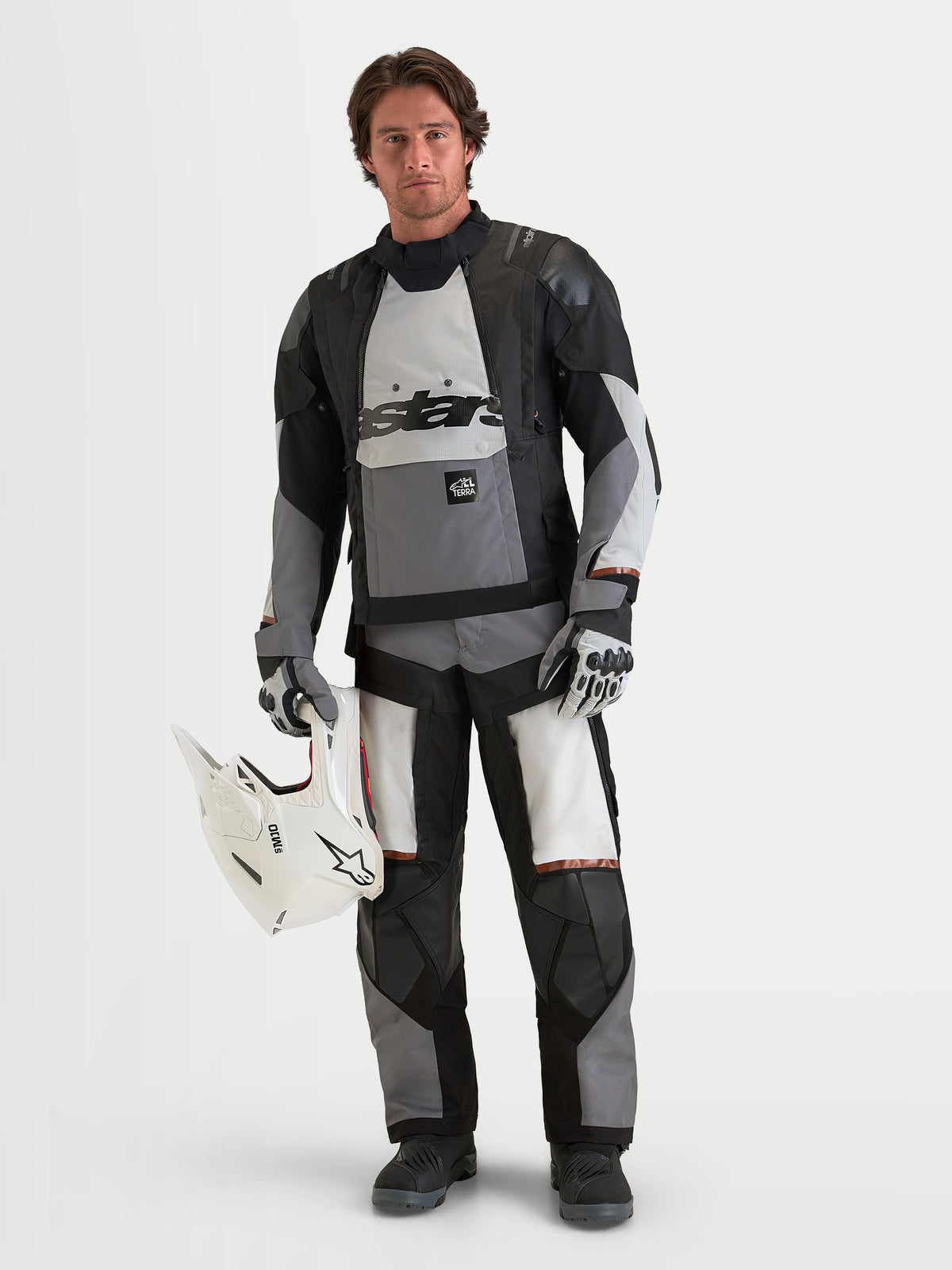 Alpinestars Harok V2 Drystar Giacca, giacca da moto adventure da uomo, grigio scuro, grigio ghiaccio e nero, struttura in tessuto impermeabile con protezione certificata CE, indossata da un modello maschile che tiene un casco bianco