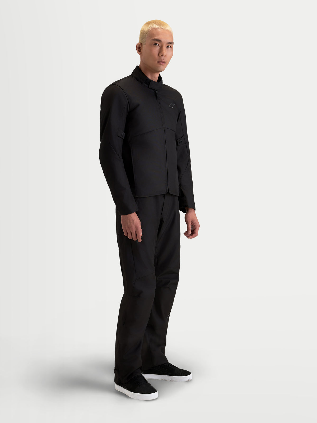 Alpinestars C 1 Waterproof Giacca, giacca da moto urbana contemporanea da uomo in nero, vista laterale su un modello che indossa pantaloni coordinati, con struttura in tessuto tecnico impermeabile e colletto con finitura morbida