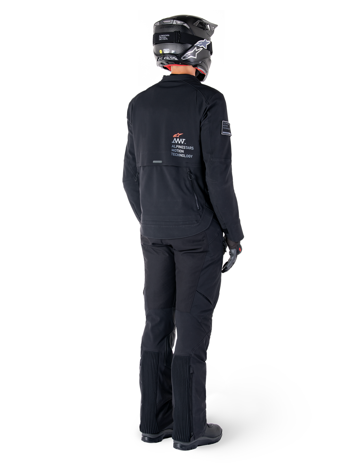 Giacca Alpinestars AMT-8 Stretch Drystar® XF, nera, vista posteriore di un pilota che indossa la giacca con pantaloni neri coordinati e un casco nero, con il marchio 'Alpinestars Motion Technology' sulla schiena, materiale tecnico elasticizzato per la guida adventure in moto