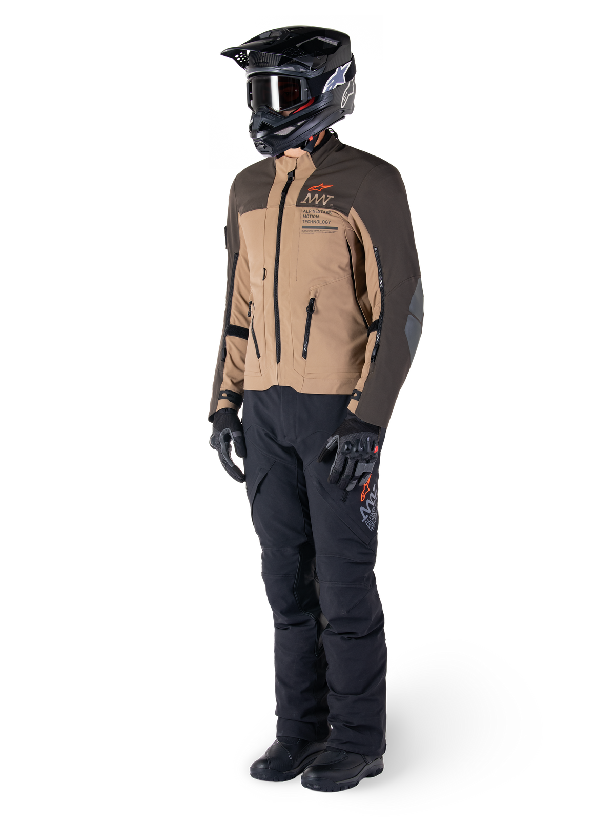 Pilota adventure con equipaggiamento completo, giacca Alpinestars AMT-8 Stretch Drystar® XF in marrone scuro e kaki scuro, abbinata a pantaloni adventure neri, casco, guanti e stivali neri, con logo AMT arancione e cerniere di ventilazione tecniche per il touring a lungo raggio