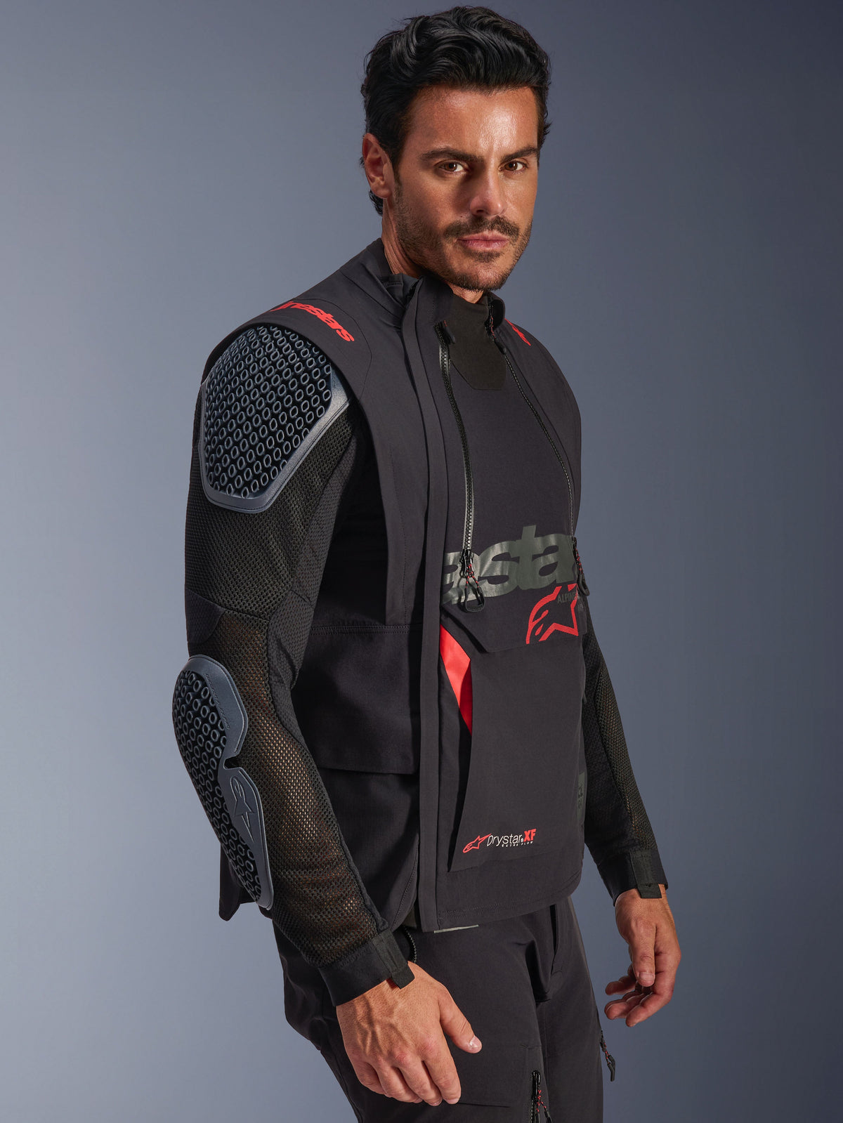 Giacca laminata Alpinestars Halo Pro Drystar® XF, nero e Dark Shadow, giacca da moto adventure indossata da un modello, configurazione modulare con maniche in rete e protezioni integrate per spalle e gomiti, accenti del logo rossi e cerniere tecniche impermeabili.