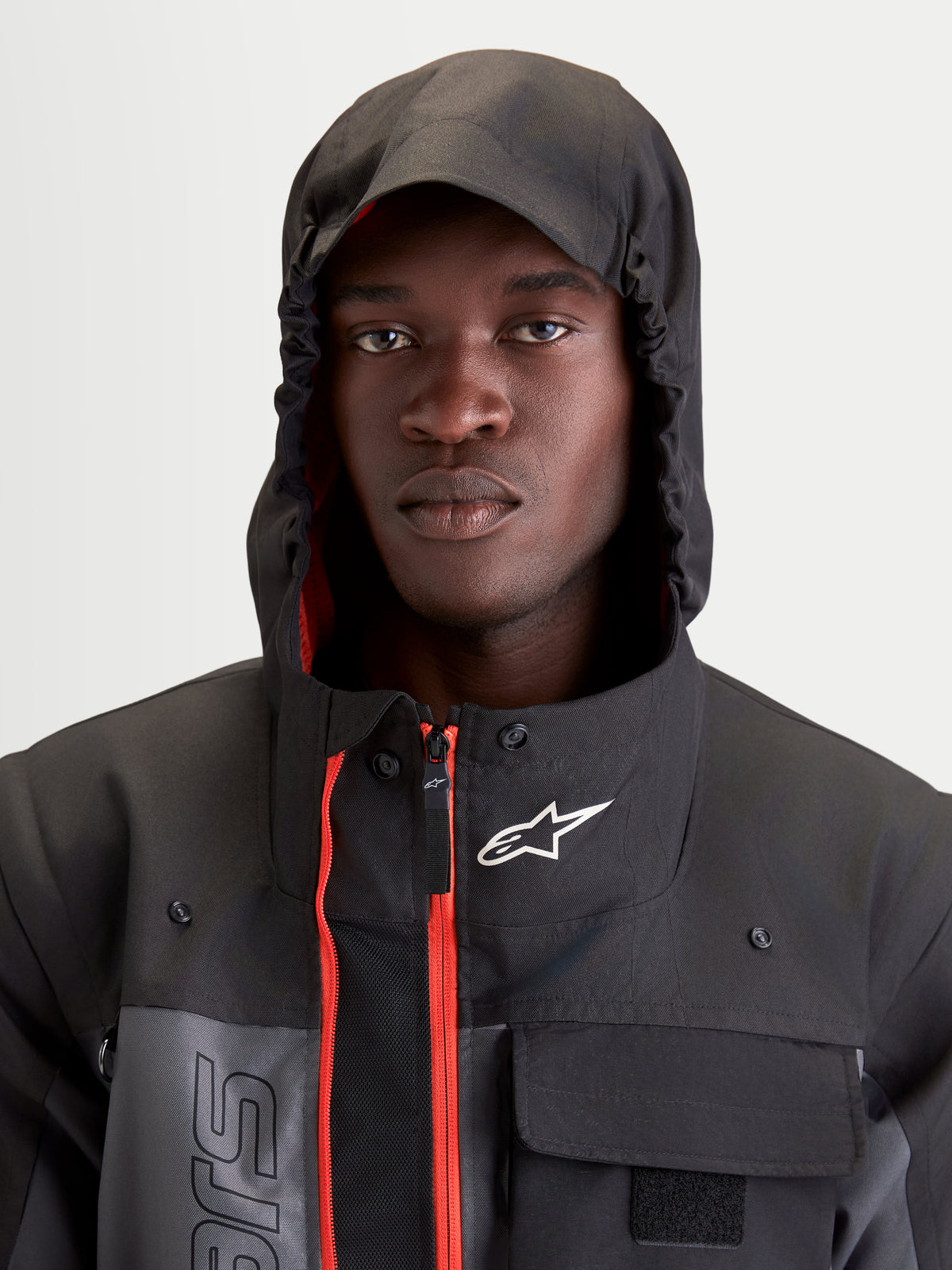 Alpinestars Morfex Parka Wp Giacca, giacca da moto urbana contemporanea da uomo in grigio lunare e nero, primo piano di un modello che indossa la giacca con cappuccio integrato sollevato e accenti interni rossi visibili