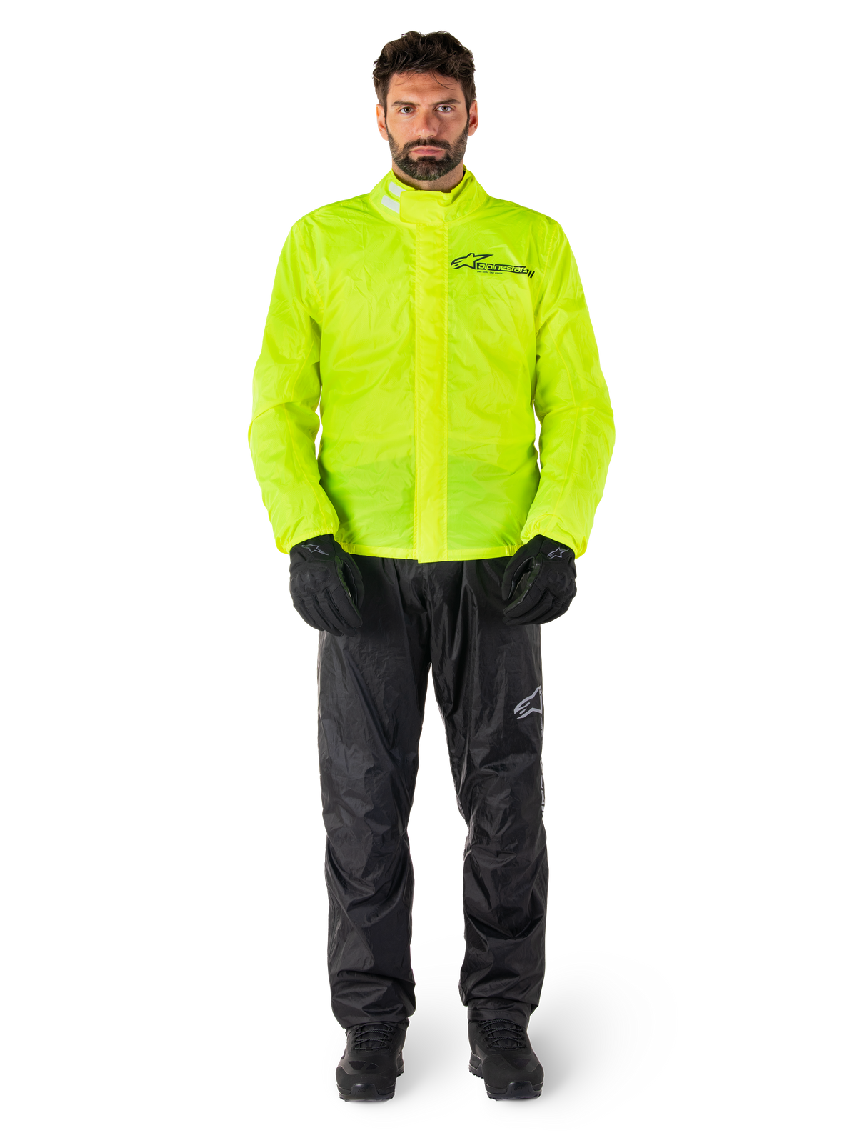 Giacca e pantaloni Alpinestars Hurricane Rain V2, giallo neon e nero, tuta antipioggia da moto impermeabile indossata con guanti e stivali neri, con il logo Alpinestars sul petto e sulla gamba
