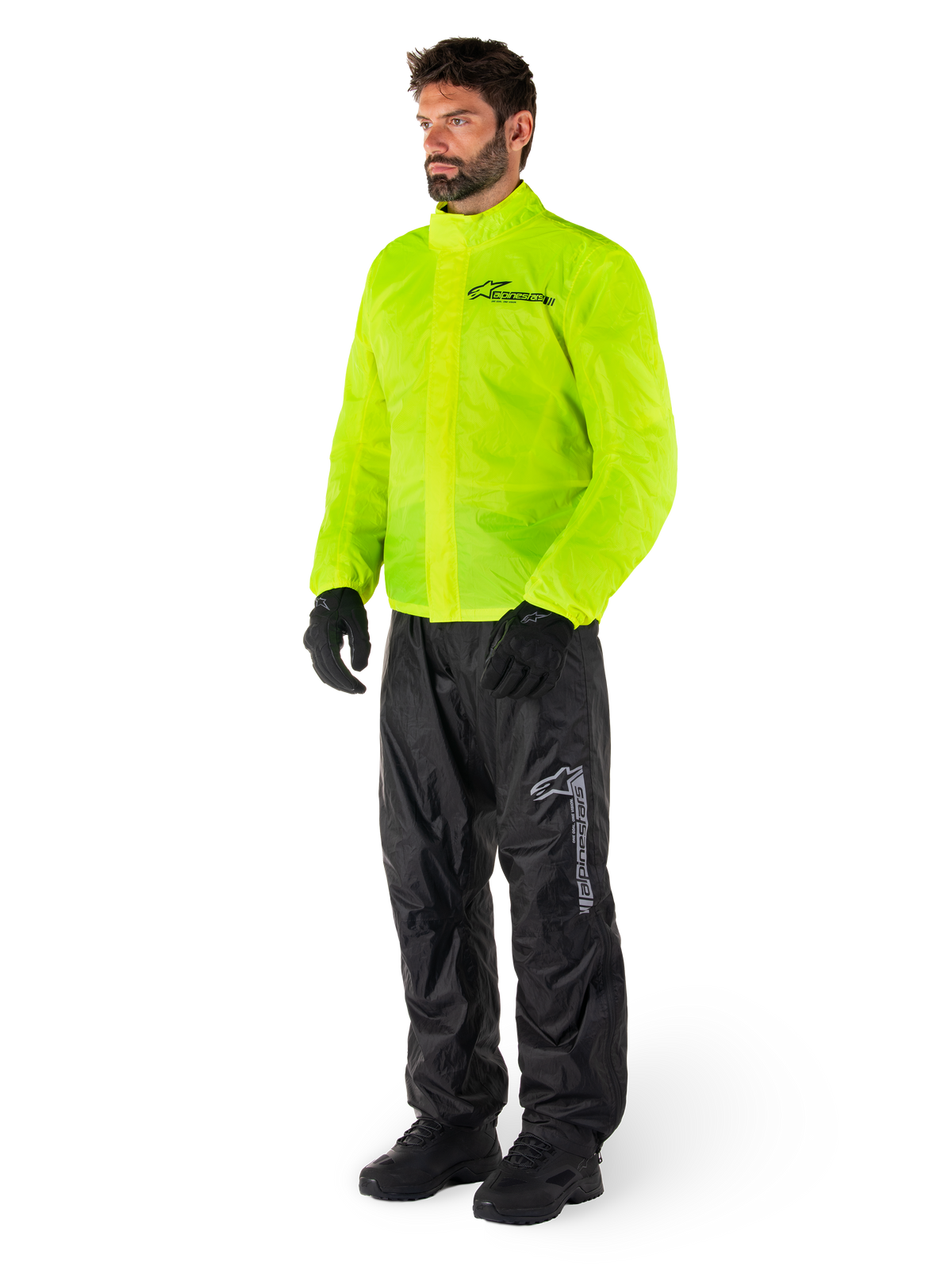 Uomo che indossa la giacca Alpinestars Hurricane Rain V2 in Giallo Fluo e i pantaloni Hurricane Rain V2 neri, abbigliamento antipioggia da moto impermeabile e ad alta visibilità, con loghi riflettenti su petto e coscia, outfit completo con guanti e stivali neri.
