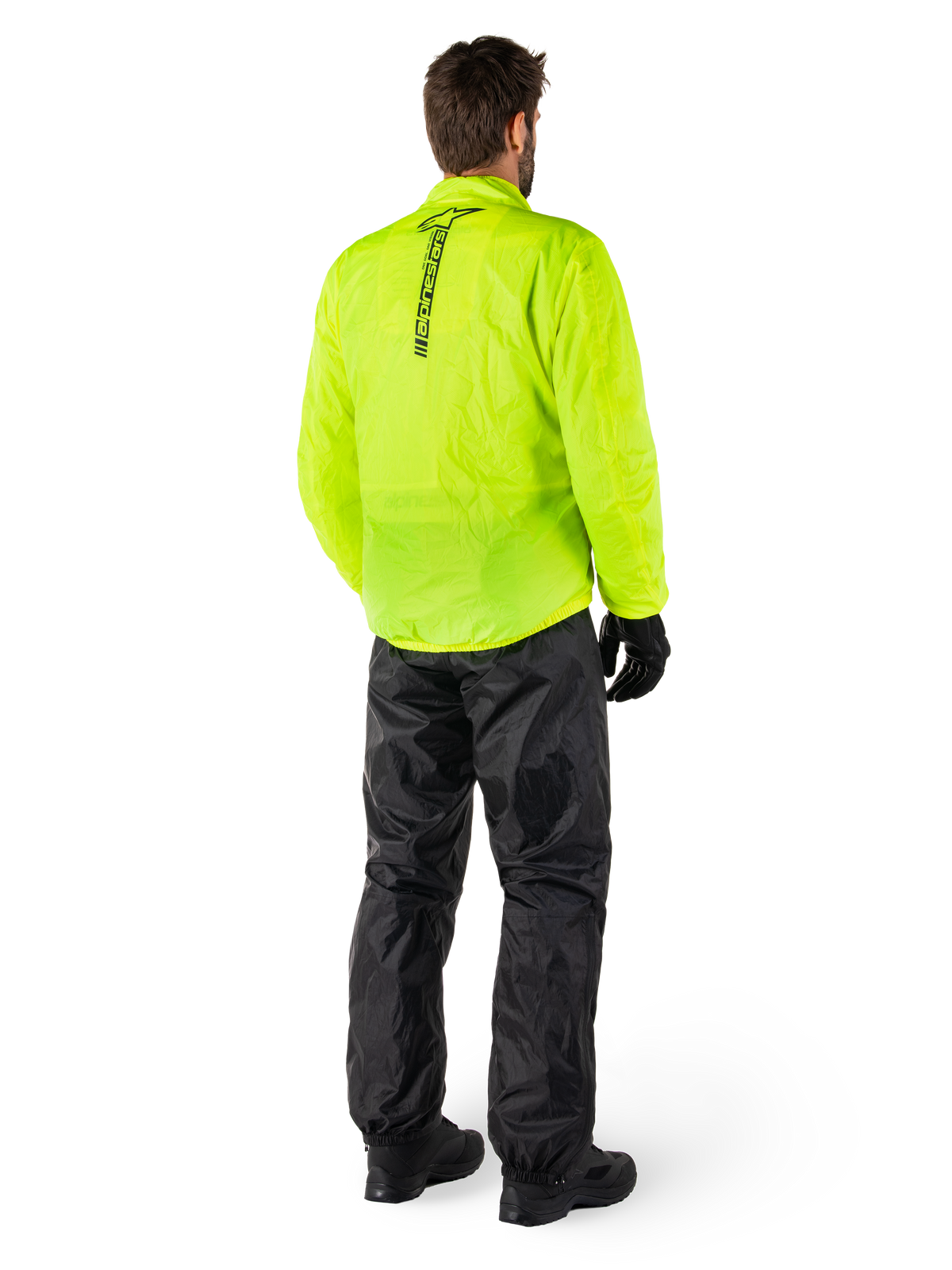 Persona vista di schiena che indossa la giacca Alpinestars Hurricane Rain V2 in Giallo Fluo e i pantaloni Hurricane Rain V2 neri, logo verticale sul retro della giacca, abbigliamento antipioggia impermeabile da moto con guanti e stivali neri