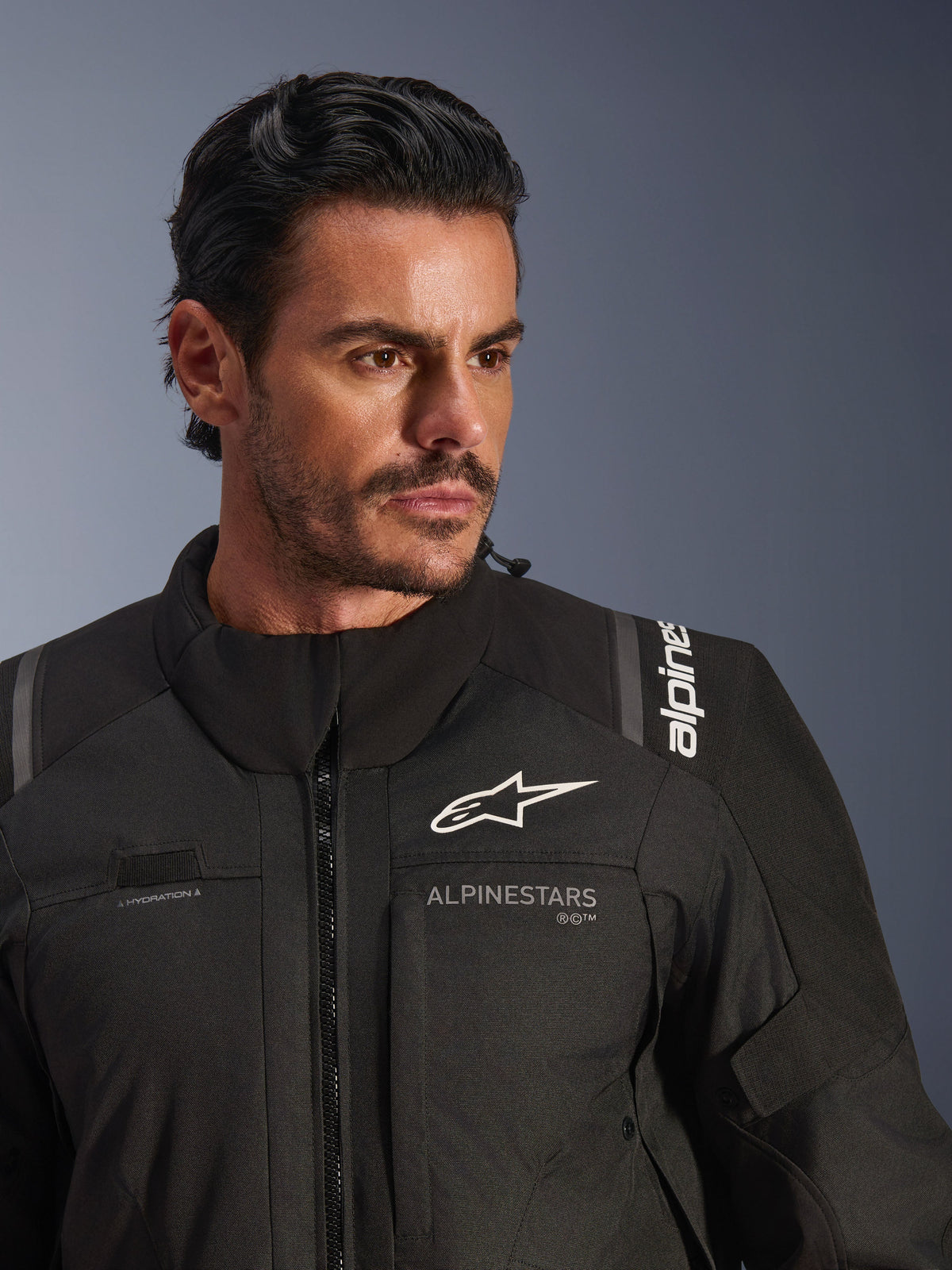 Giacca Alpinestars Andes V4 Drystar®, nero, indossata da un modello, primo piano su petto e spalle, con loghi Alpinestars bianchi, materiale tessile con dettagli di ventilazione e asola per tubo di idratazione, abbigliamento da moto adventure-touring
