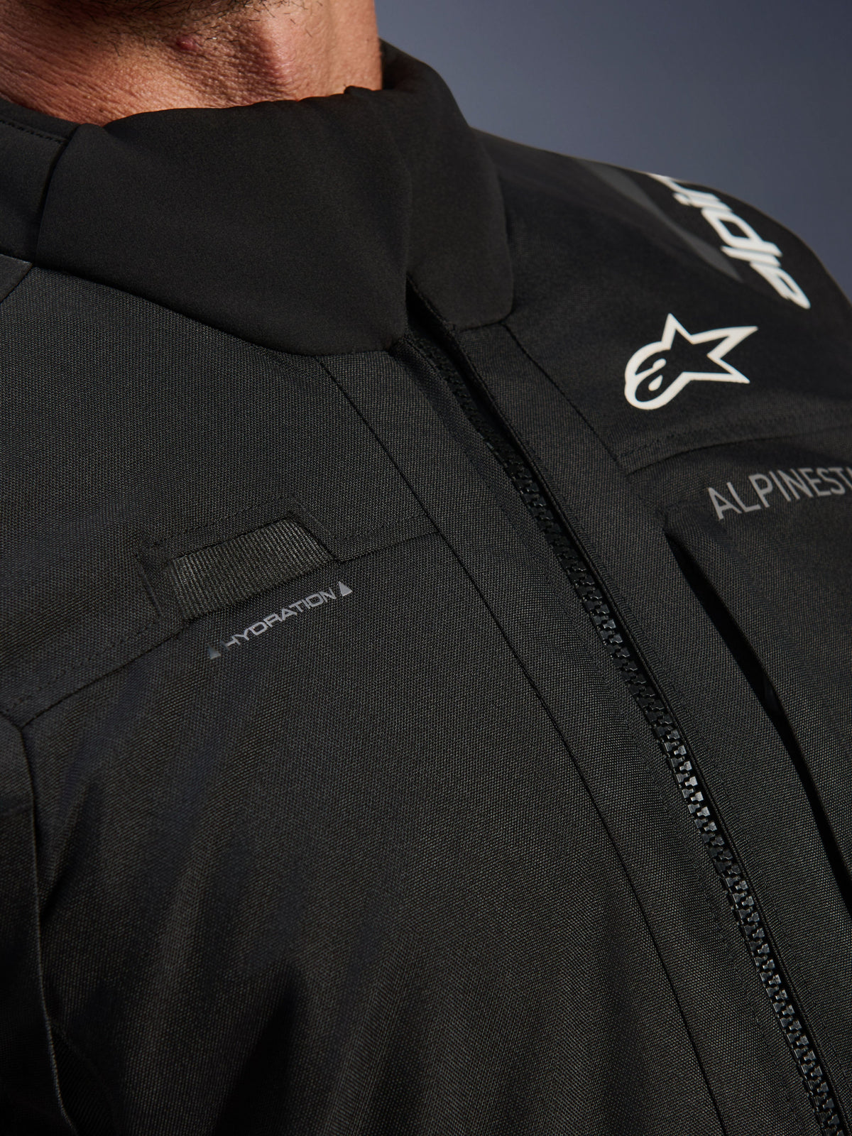 Giacca Alpinestars Andes V4 Drystar®, nera, primo piano del dettaglio del petto con passante per il tubo di idratazione, cerniera anteriore VISLON® impermeabile e logo Alpinestars su materiale tessile resistente